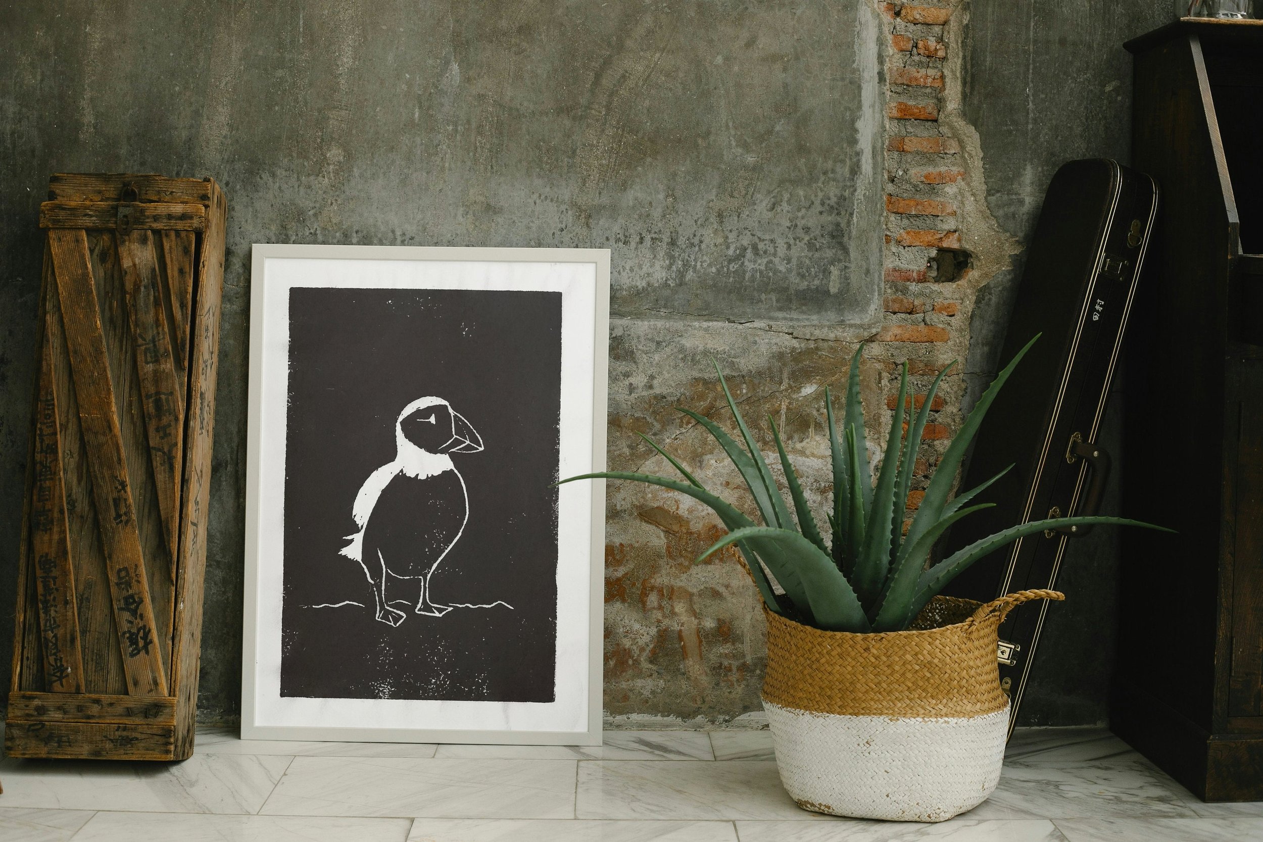 A puffin lino cut print displayed beside a modern planter with lush greenery, against a textured wall.