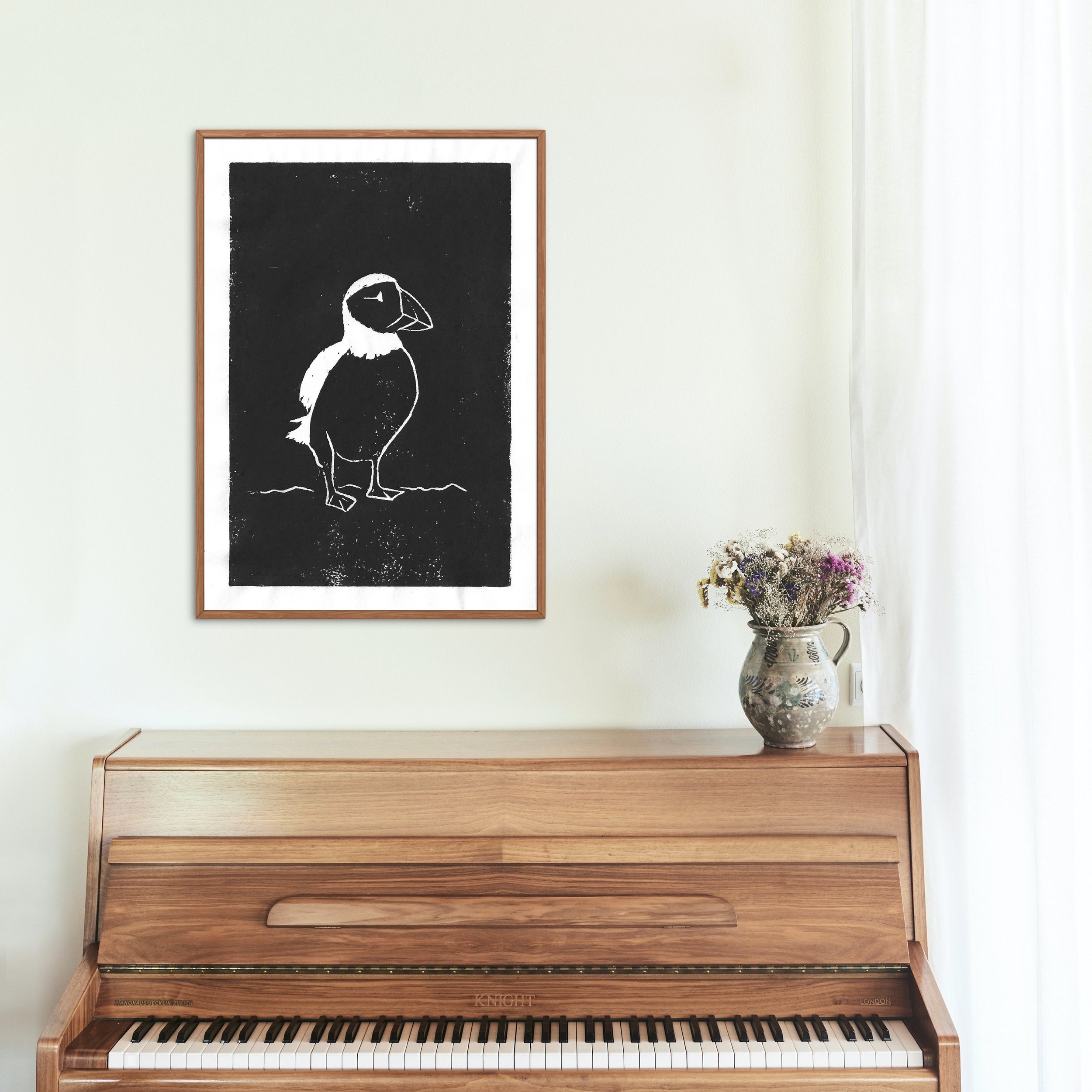 The puffin artwork is framed and styled above a sleek wooden piano, paired with simple, rustic decor.