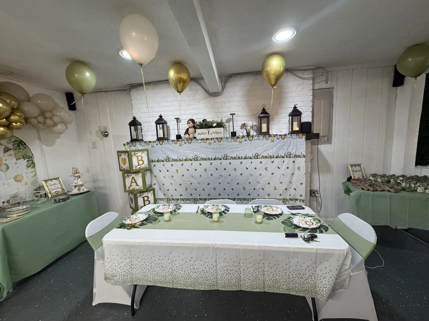 Sage and white head table with gold and olive balloons and brass lanterns at a baby shower