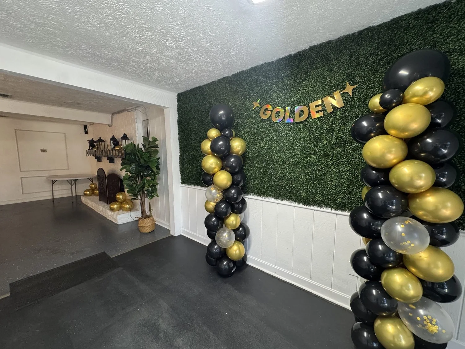 Black and gold balloon columns with a GOLDEN banner on the greenery wall