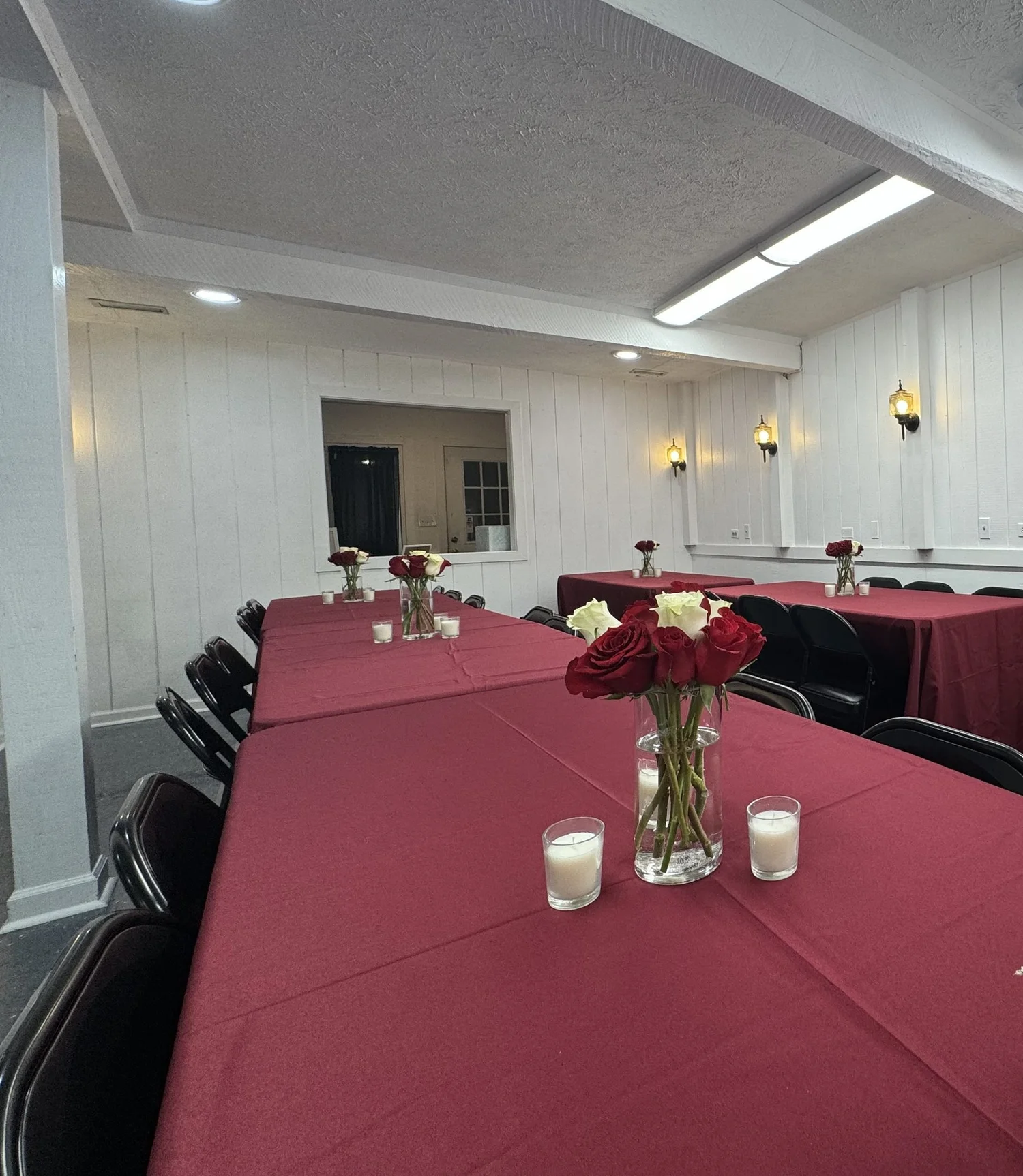 Long tables with burgundy linens, black chairs and red and white rose centerpieces set for a bridal shower