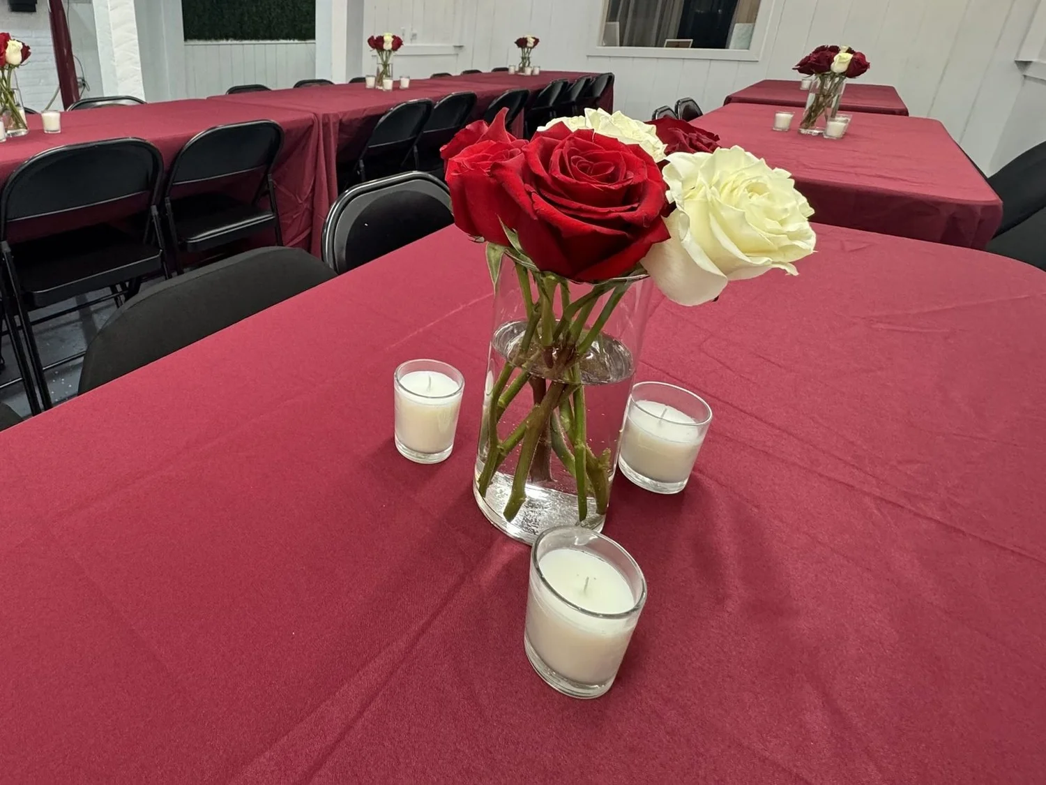 Red and white rose centerpiece with candles on a burgundy-draped table, set for a bridal shower at The Spot 757