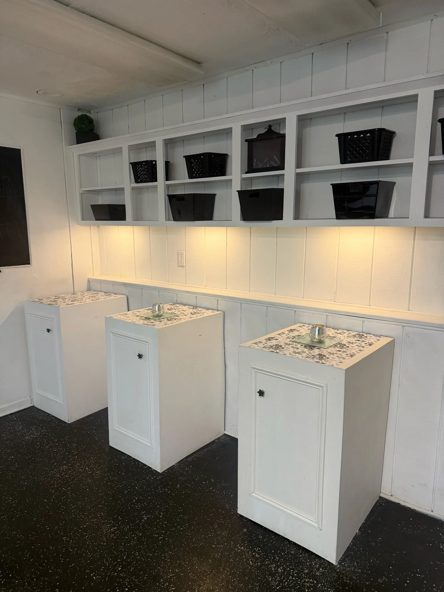 Catering room with white cabinet counters, open shelving with black baskets and under-shelf lighting