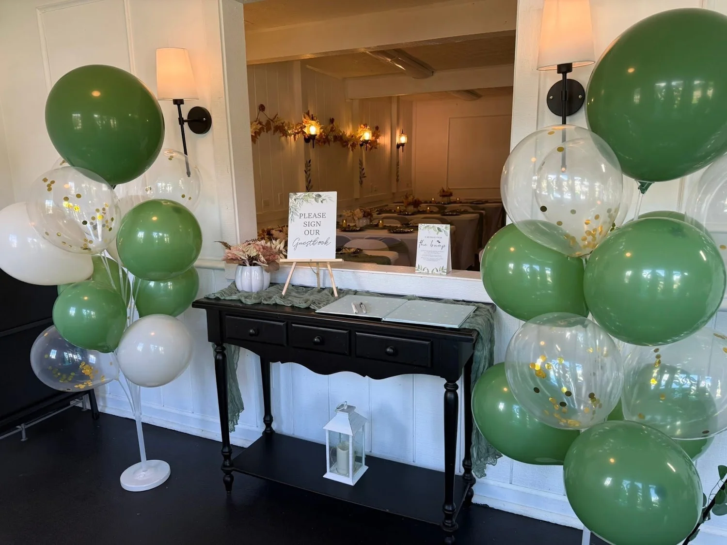 Entry console table framed by sage green and clear balloon columns, set dining room behind
