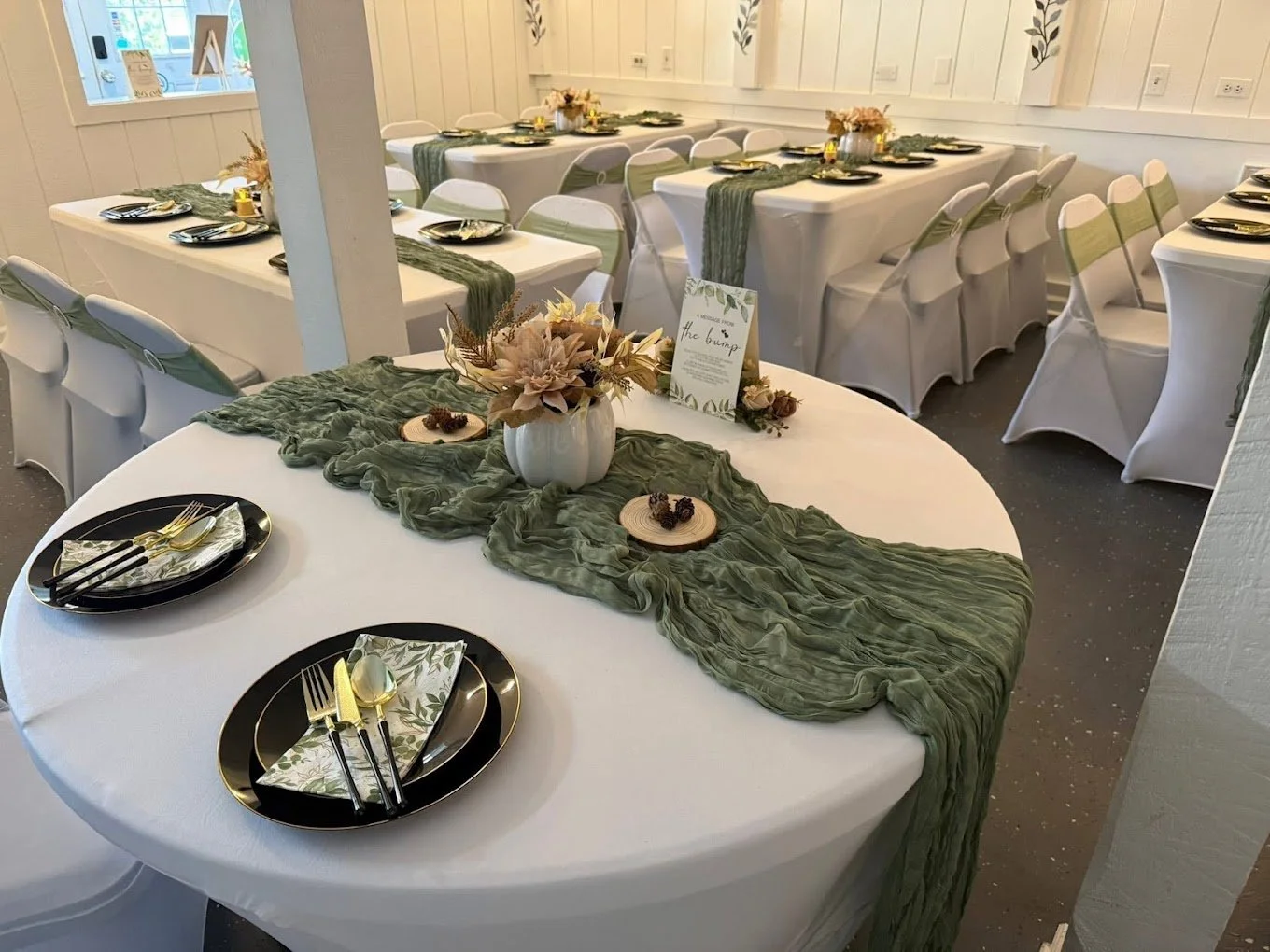 Round table with white linen, sage runner, black plates and gold flatware