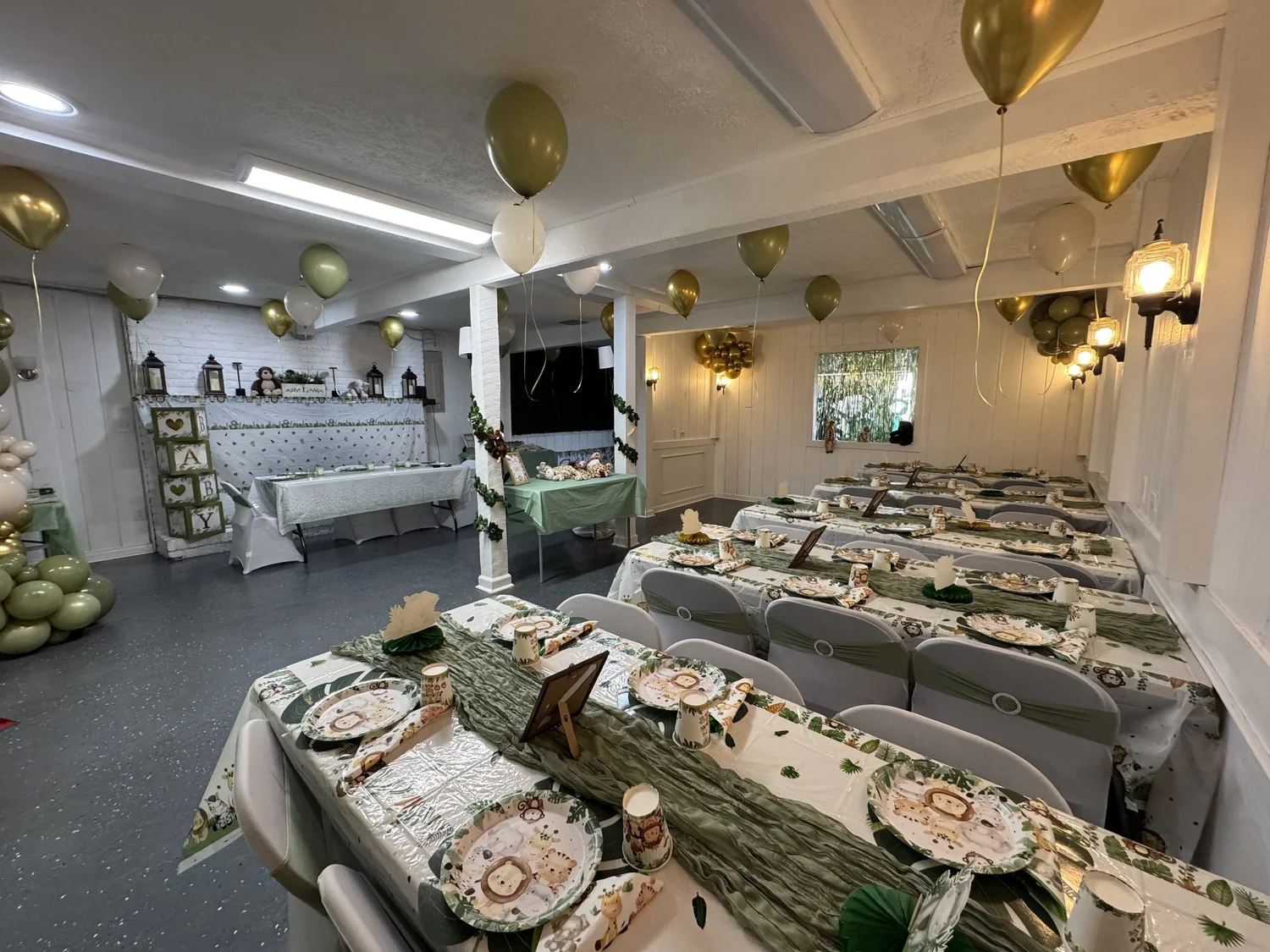 Main room set for a sage and gold baby shower, long tables with greenery runners and gold balloons