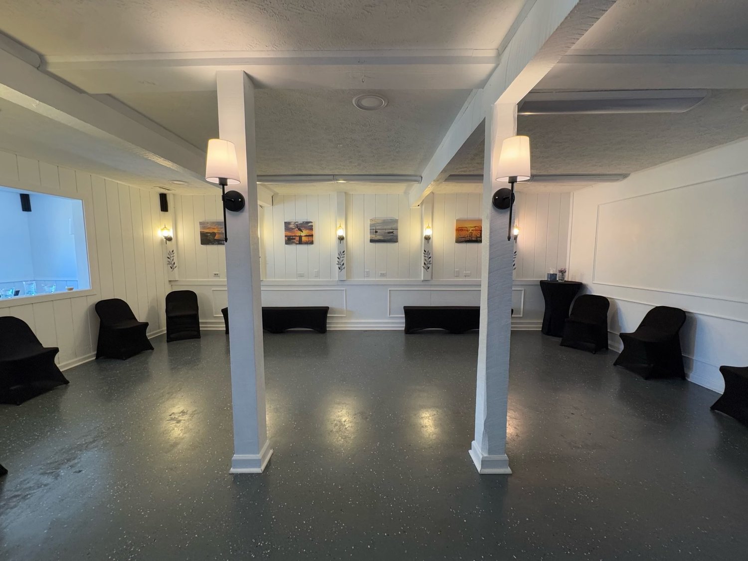 Open floor with white columns, wall sconces, framed sunset art and black lounge seating along the paneled walls