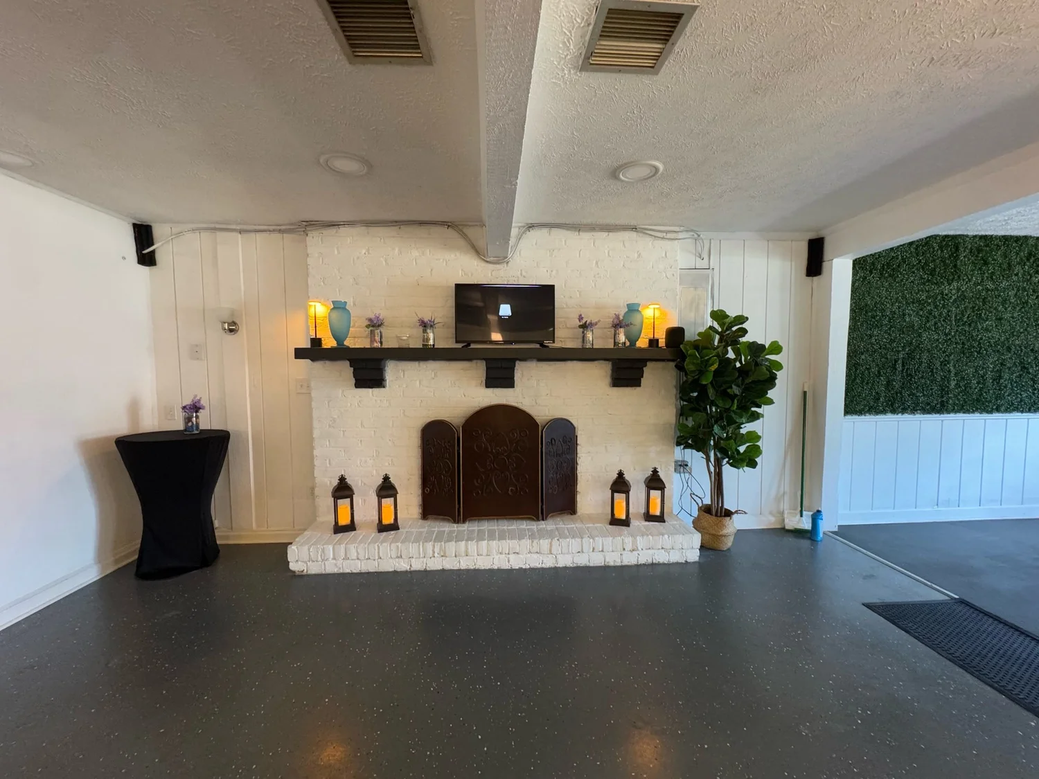 White brick fireplace with lanterns, blue vases and lamps on the mantel, a fiddle leaf fig, and the foyer greenery wall through the doorway