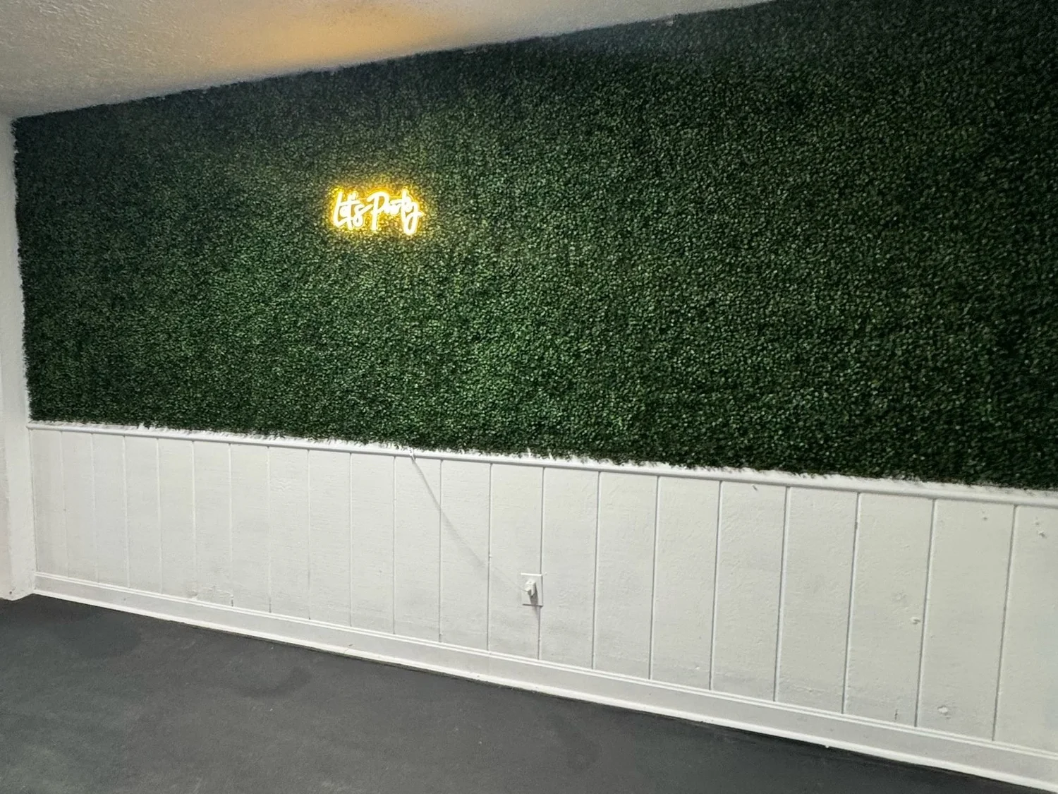Boxwood greenery wall in the foyer with a warm Let's Party neon sign above white wainscoting