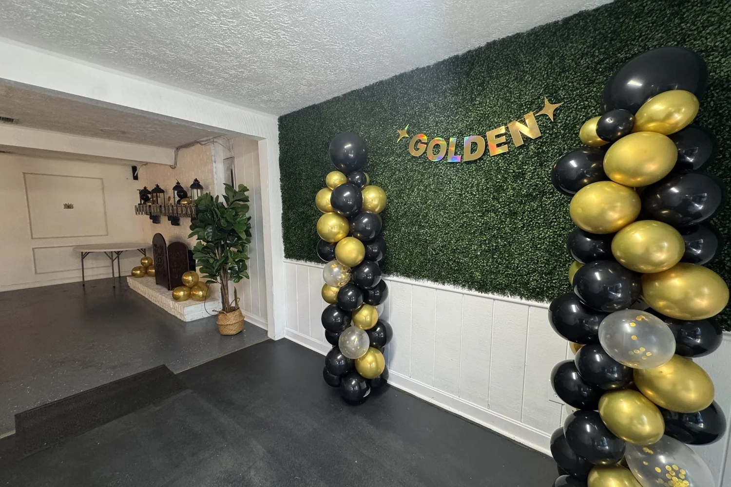 Black and gold balloon columns and a gold "Golden" banner on the foyer greenery wall for a birthday party