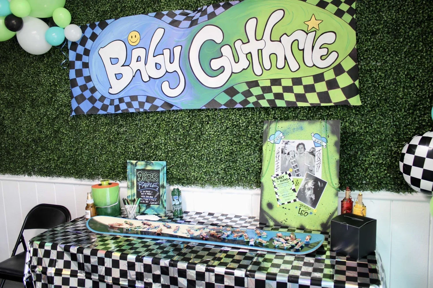 "Baby Guthrie" racing-theme baby shower table with checkered linens in front of the greenery wall