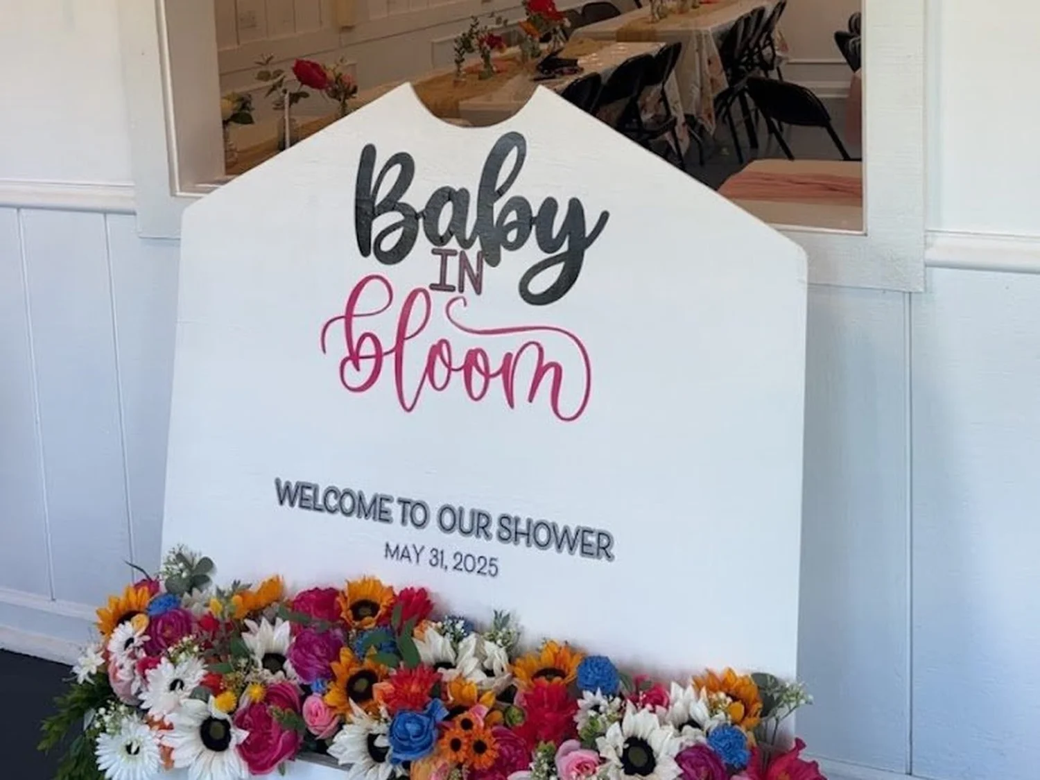White wooden "Baby in Bloom" welcome sign with a planter of bright flowers, set up for a baby shower at The Spot 757