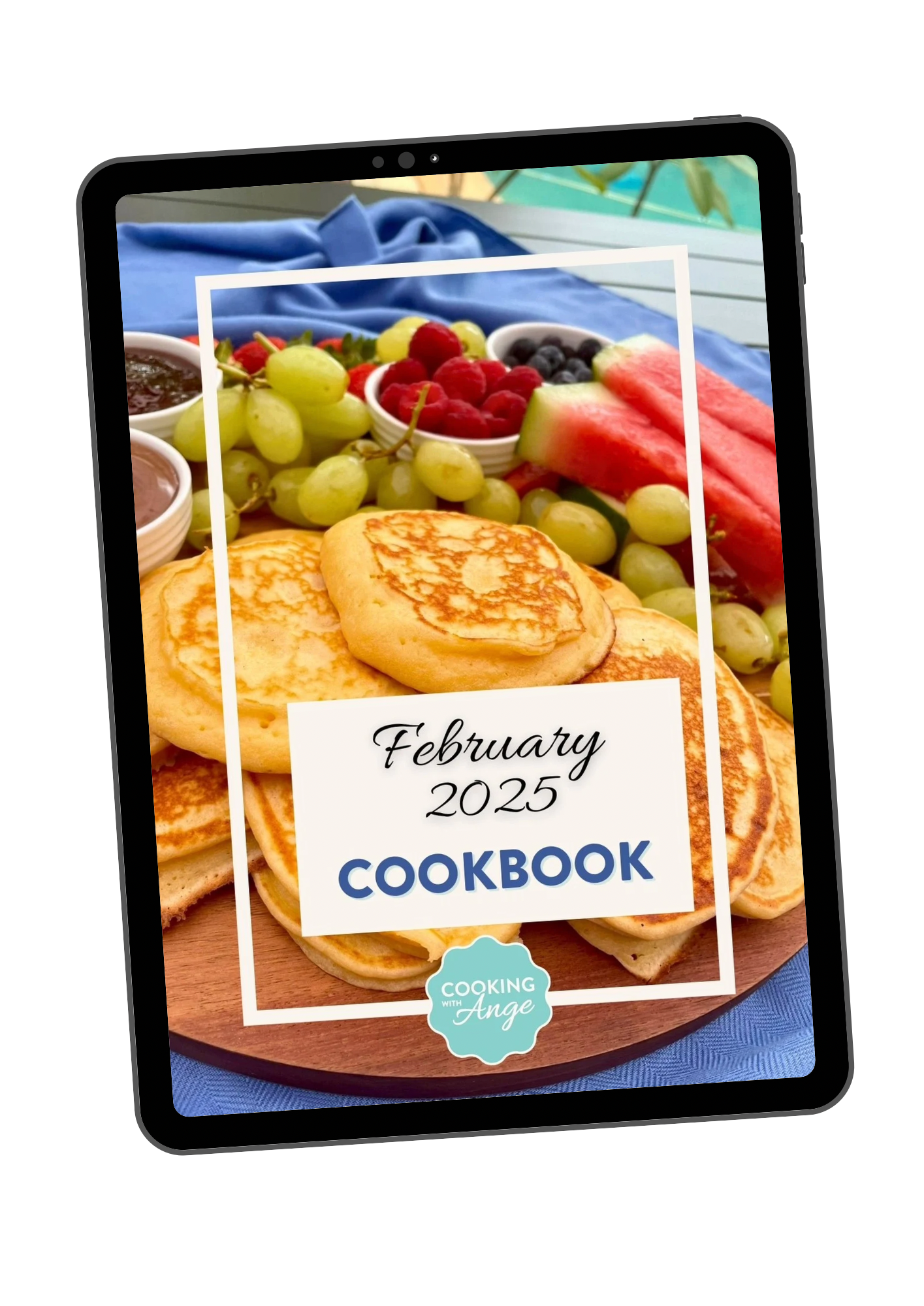 Tablet displaying 'February 2025 Cookbook' cover featuring pancakes, grapes, watermelon slices, raspberries, blueberries, and small bowls of sauces.