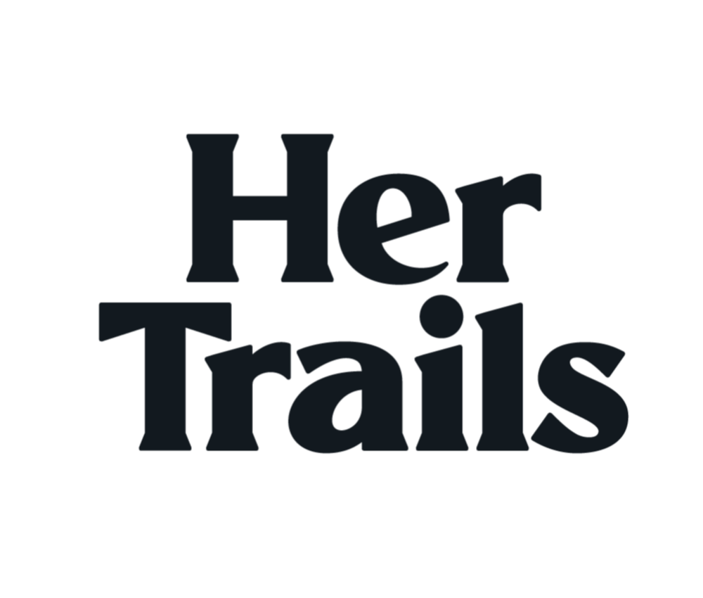 Text graphic reading 'Her Trails' with a silhouetted bicycle and mountain background.