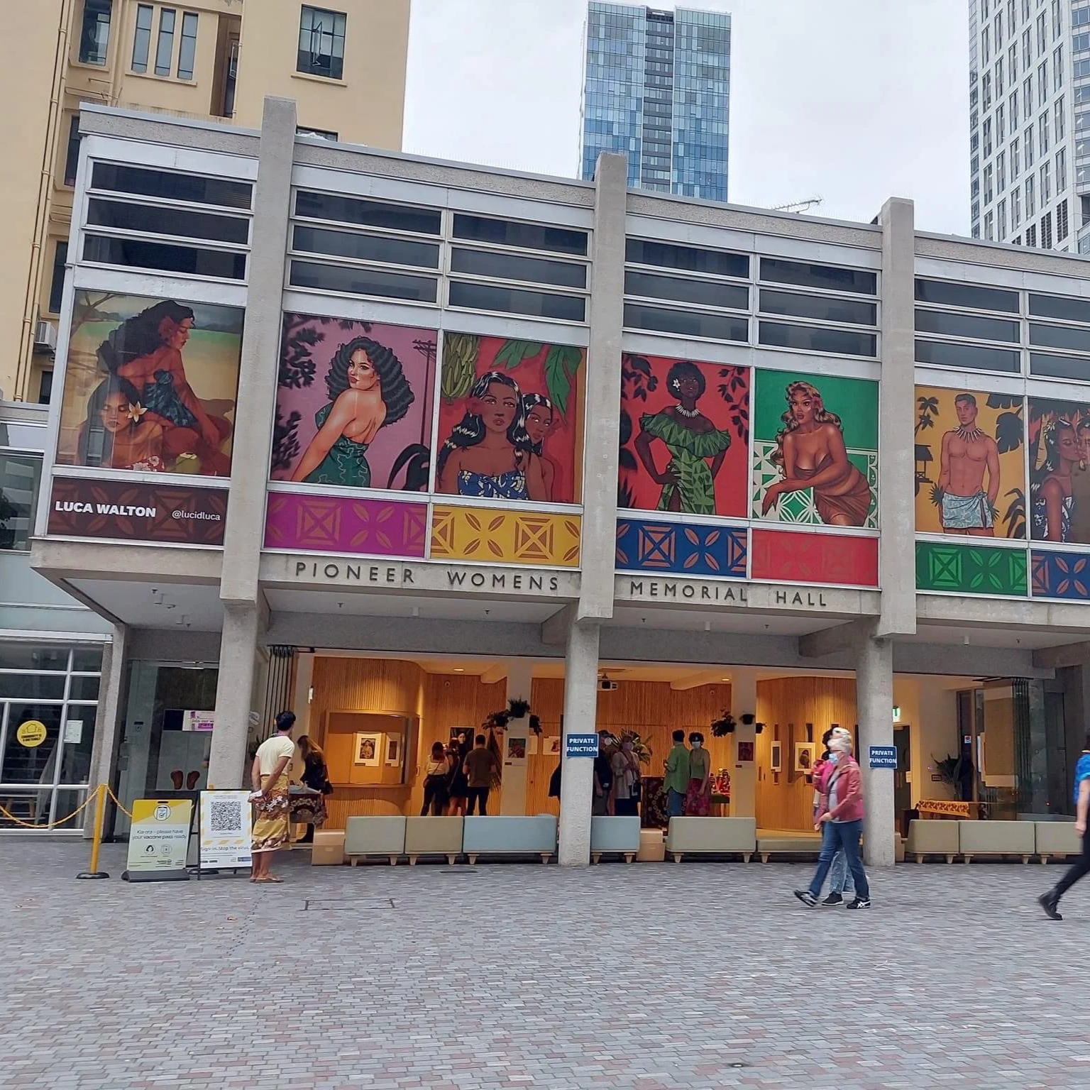People walking near the entrance of Pioneer Women Memorial Hall with colorful artwork of women on the building's facade.