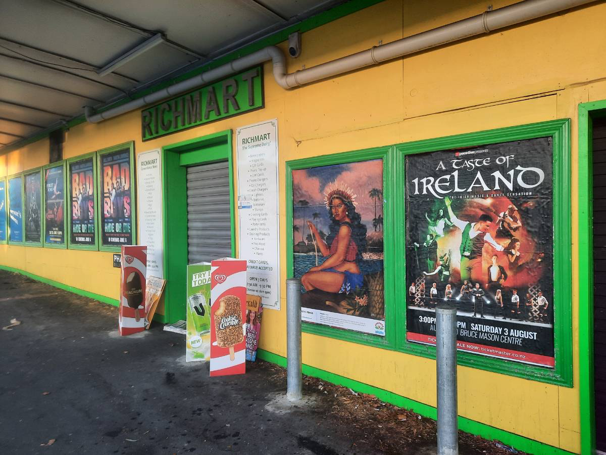 Exterior of a building with yellow walls and green framing, advertisements for movies, and posters promoting Irish music and dance. There are also signs and ice cream advertisements outside the entrance.