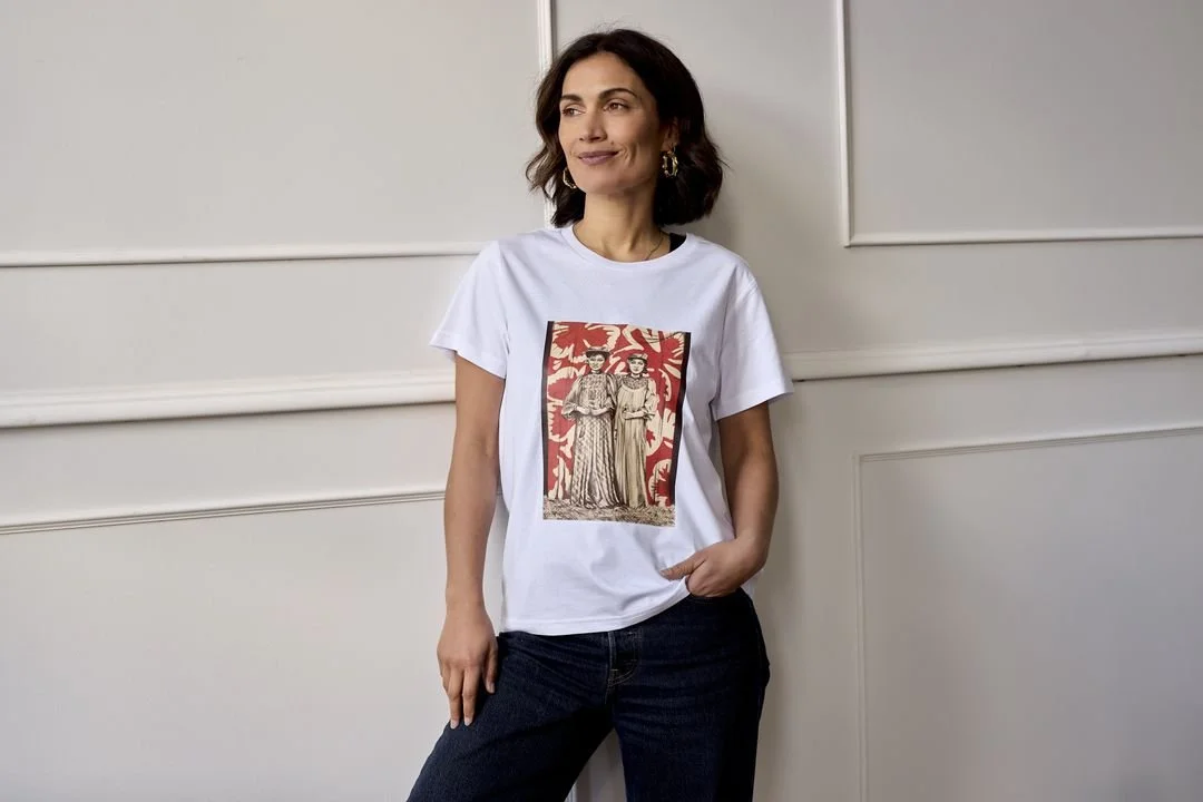 Woman wearing a white T-shirt with a graphic print, standing against a white wall.
