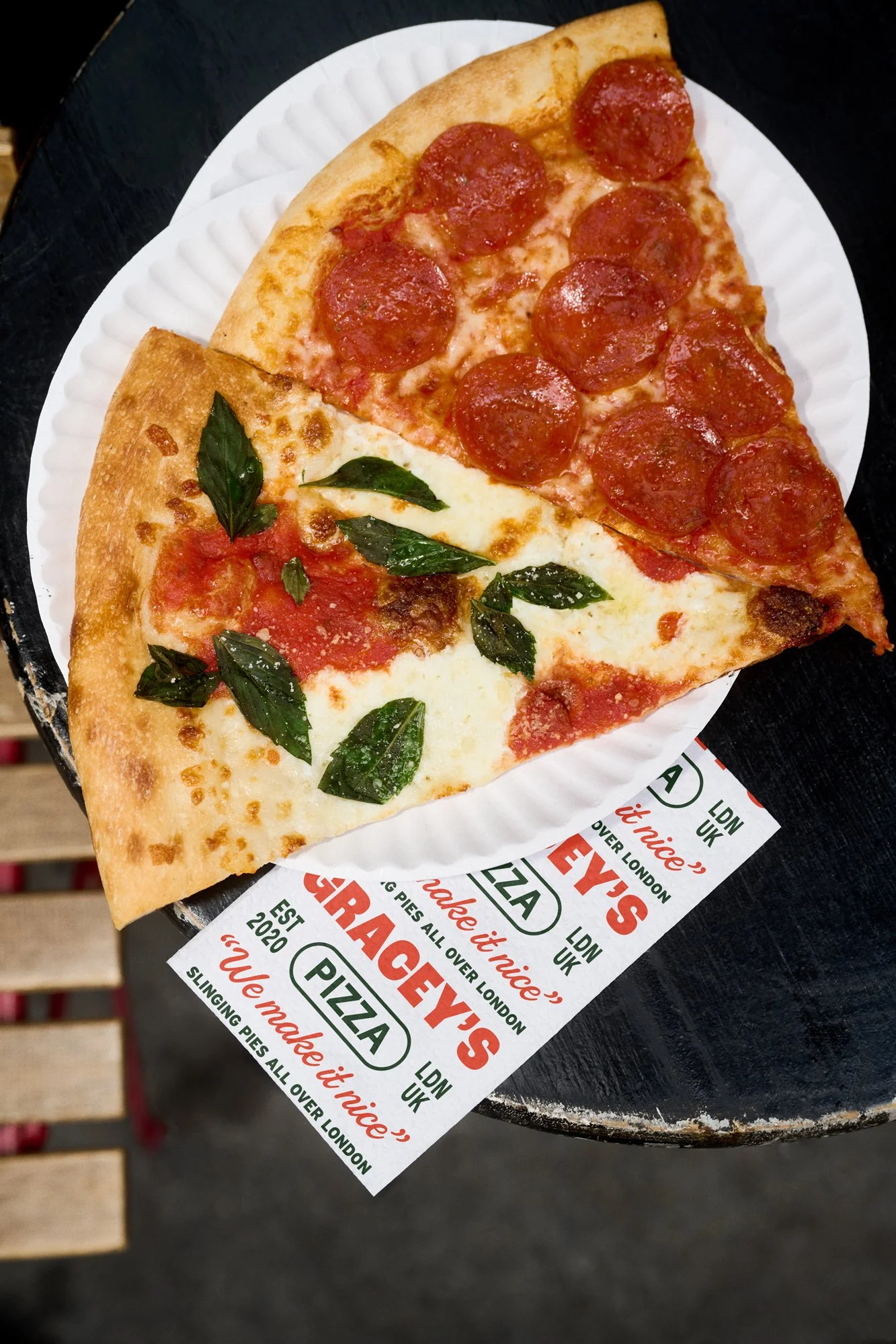 A slice of pizza with pepperoni, cheese, and tomato sauce, garnished with basil leaves on a paper plate.