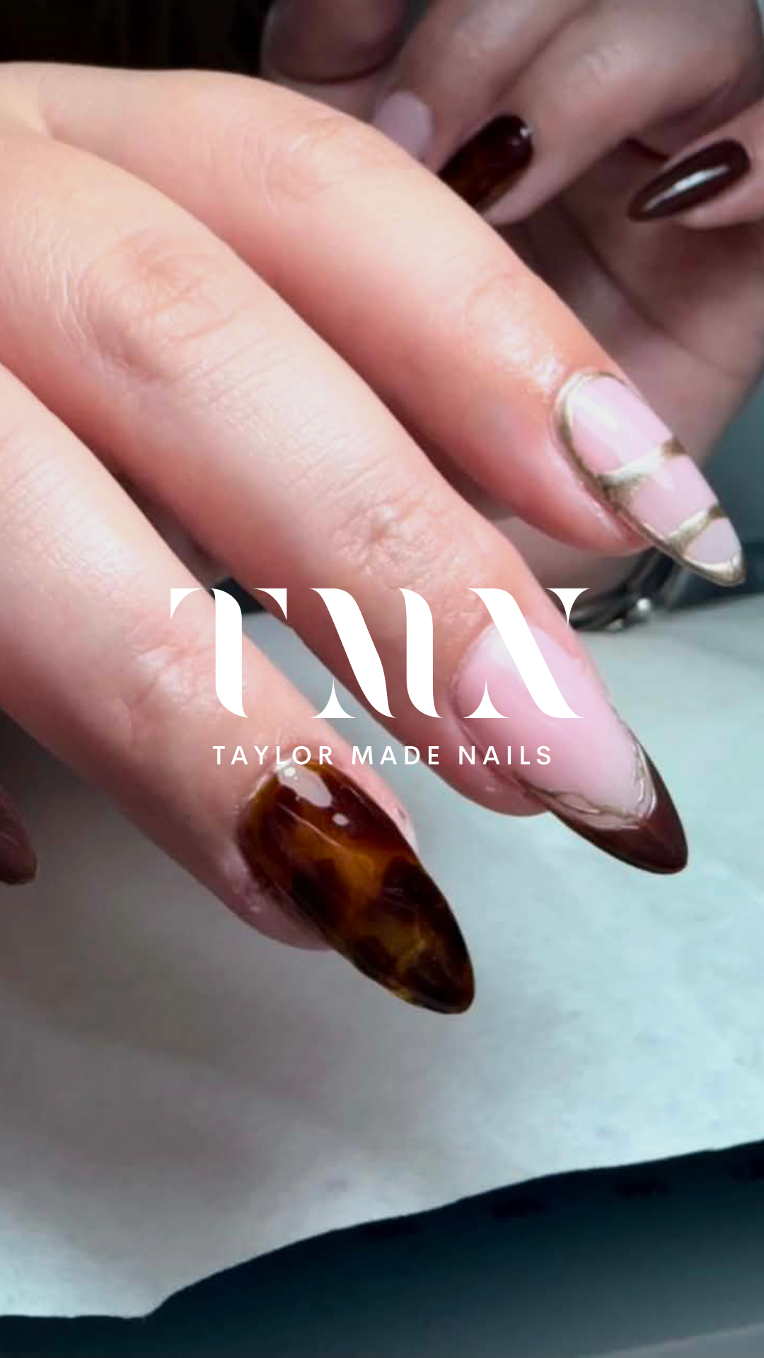 Close-up of a hand with manicured nails featuring a taupe and brown marble design, with the text 'TAYLOR MADE NAILS' overlayed.