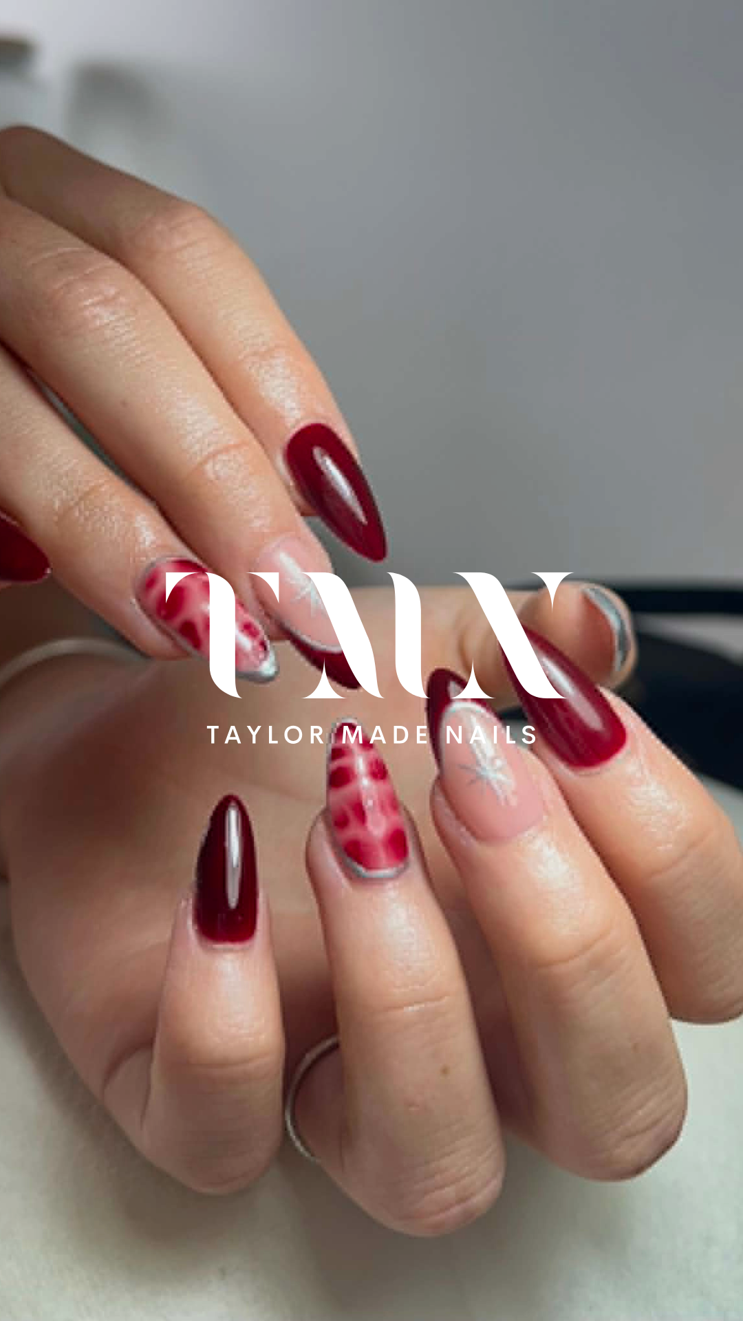 Close-up of hands displaying manicured nails with red, white, and pink geometric and floral nail art, with the text 'TAYLOR MADE NAILS' overlaid.