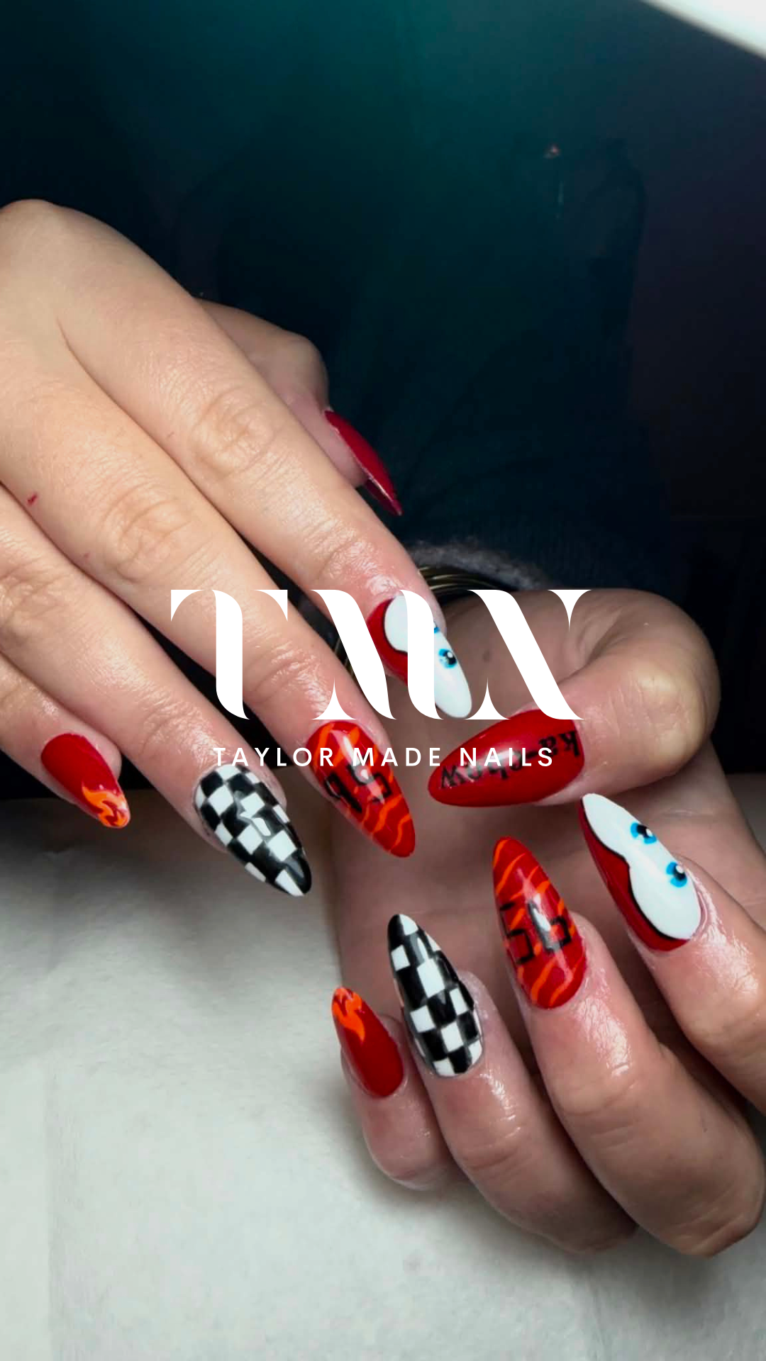 Close-up of a person's hand with colorful, patterned acrylic nails featuring various designs including checkered, flames, and cartoon eyes.