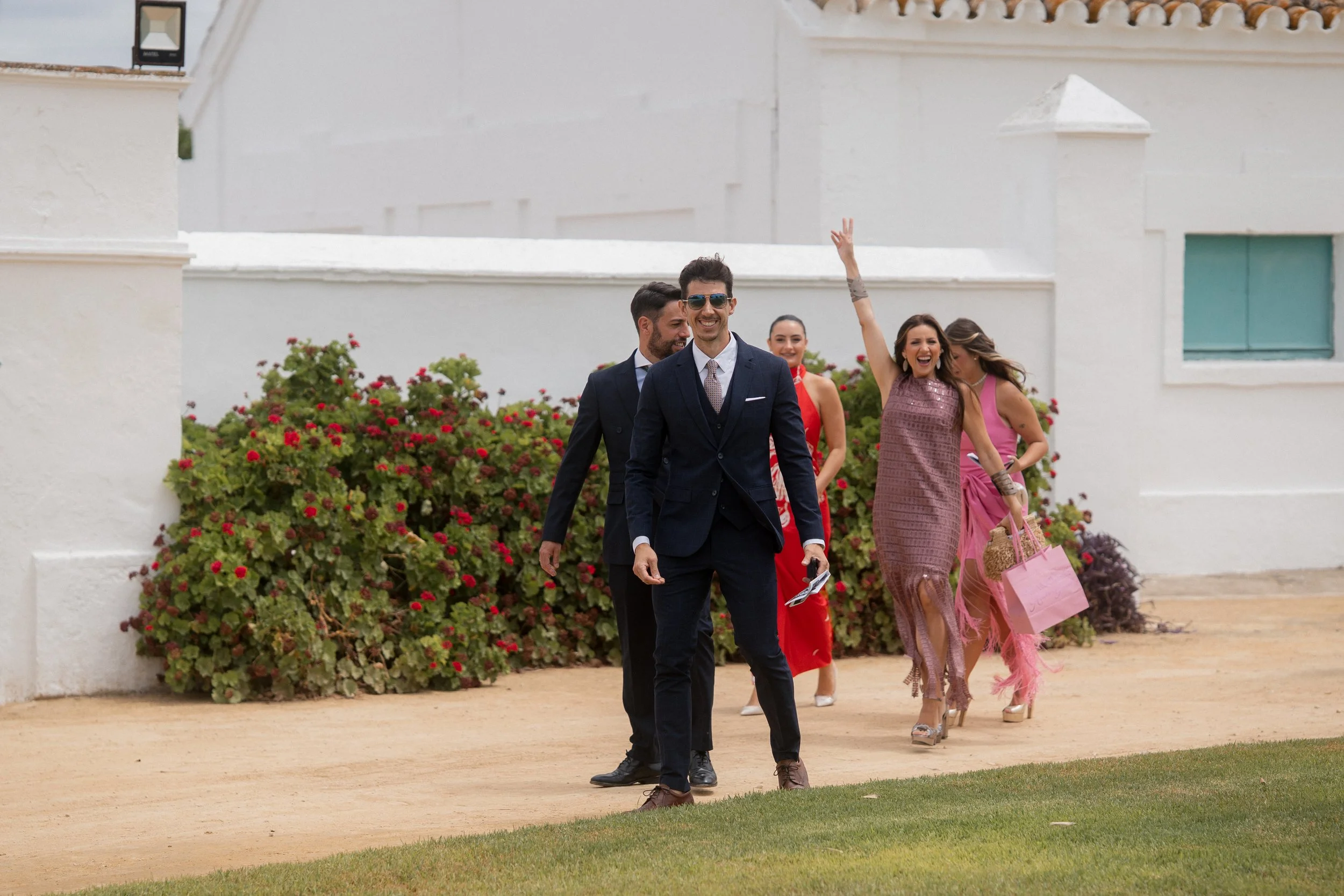 Grupo de personas vestidas con ropa elegante caminando en un jardín, sonriendo y disfrutando del día.