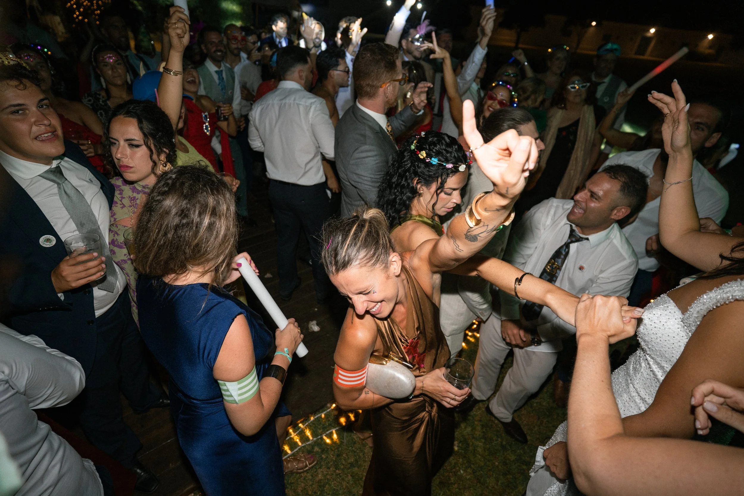 Personas bailando y disfrutando en una fiesta, en un lugar con iluminación nocturna, algunos con accesorios coloridos y ropa elegante.