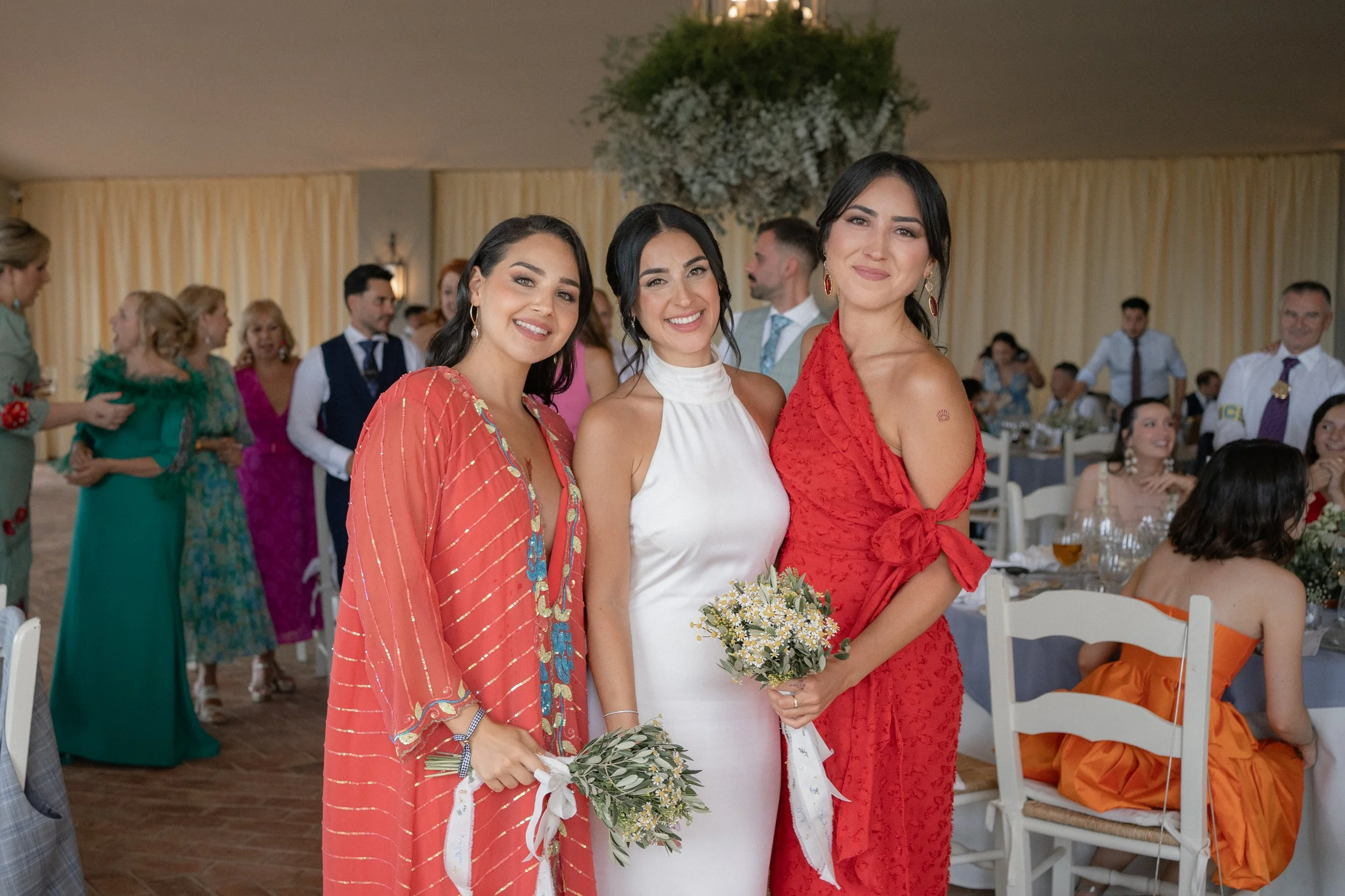 Tres mujeres en vestido de novia y trajes de color rojo en una ceremonia en un salón de eventos.