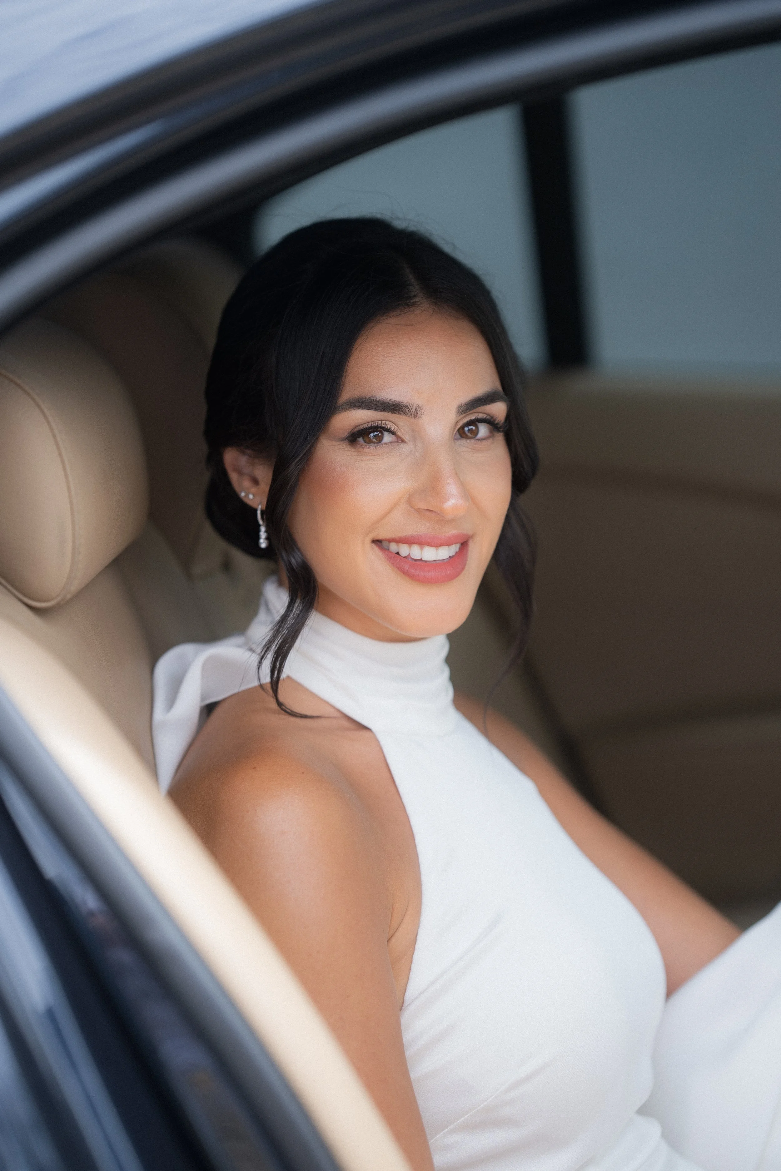 Novia con vestido de pronovias blanco y pendientes, sonriendo hermosa en el interior de un coche de bodas.