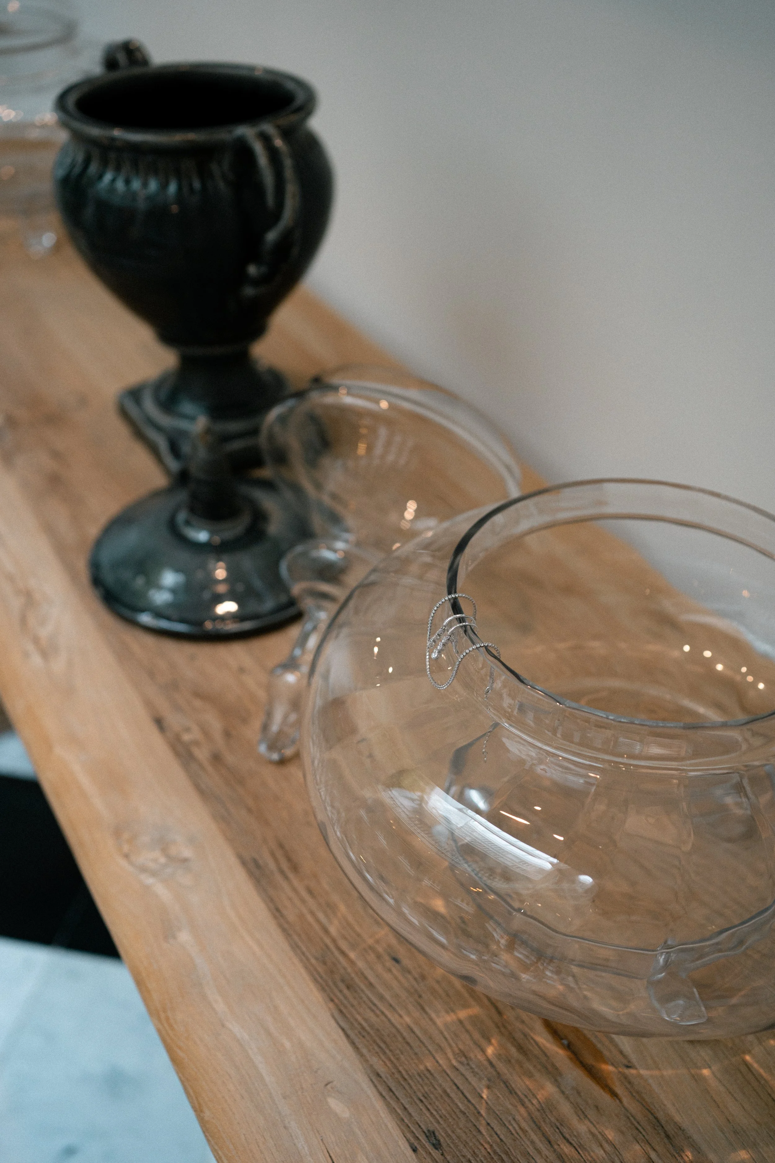 Vasos y copas de cristal y un jarrón de cerámica negra sobre una mesa de madera.