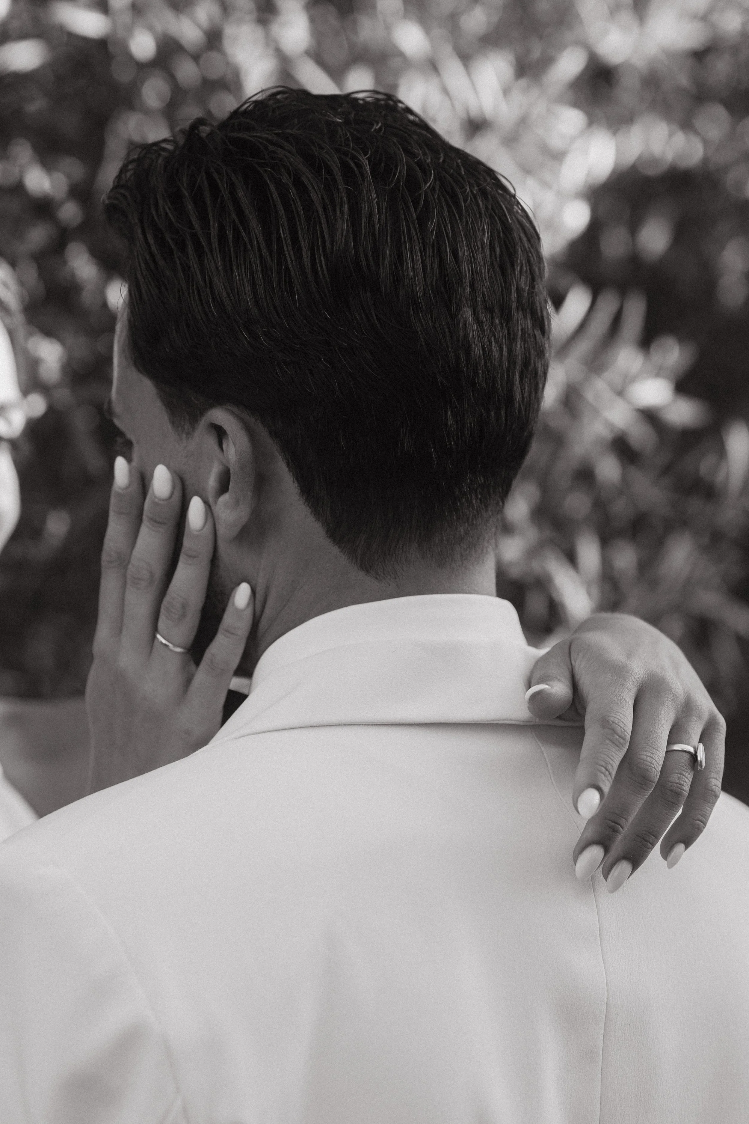 Pareja abrazada y tocándose la cara y el hombro, vista desde atrás, en un entorno natural.