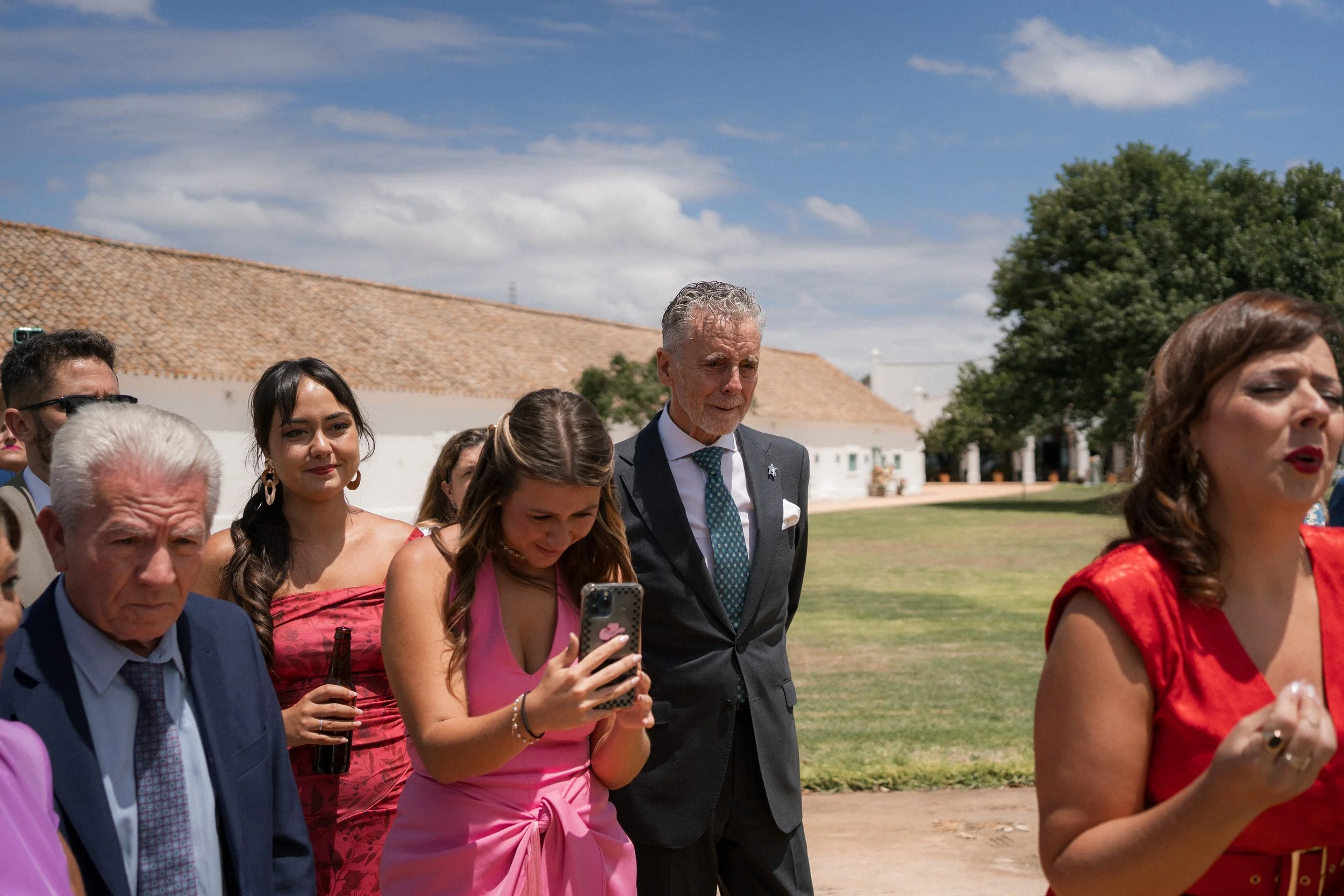 Grupo de personas en una reunión al aire libre en un día soleado, entre ellos Faly Pastrana, con edificios tradicionales y árboles en el fondo.