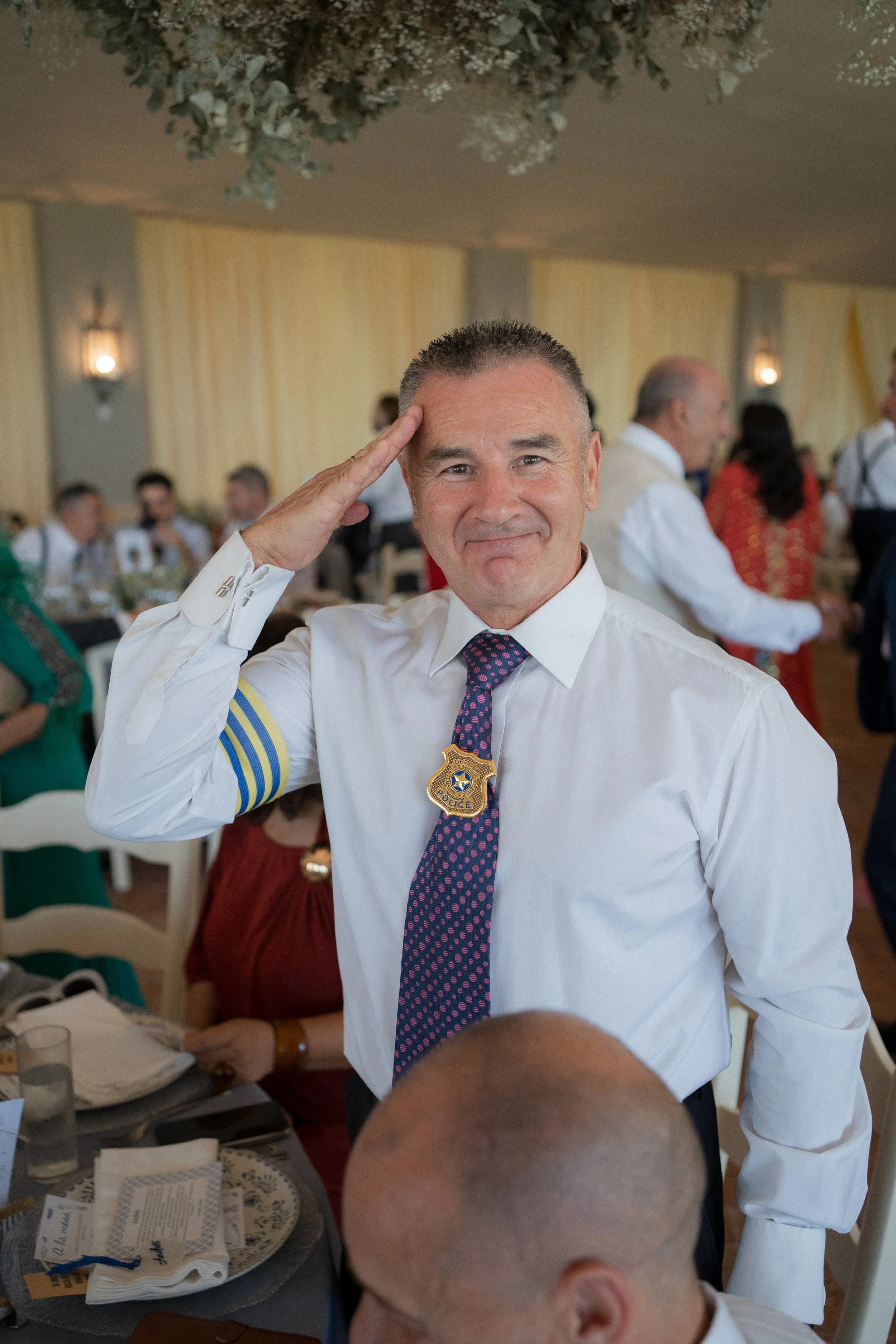 Invitado de una boda, saluda con la mano derecha en una celebración en un banquete en Dehesa Bolaños decorado con cortinas y flores.