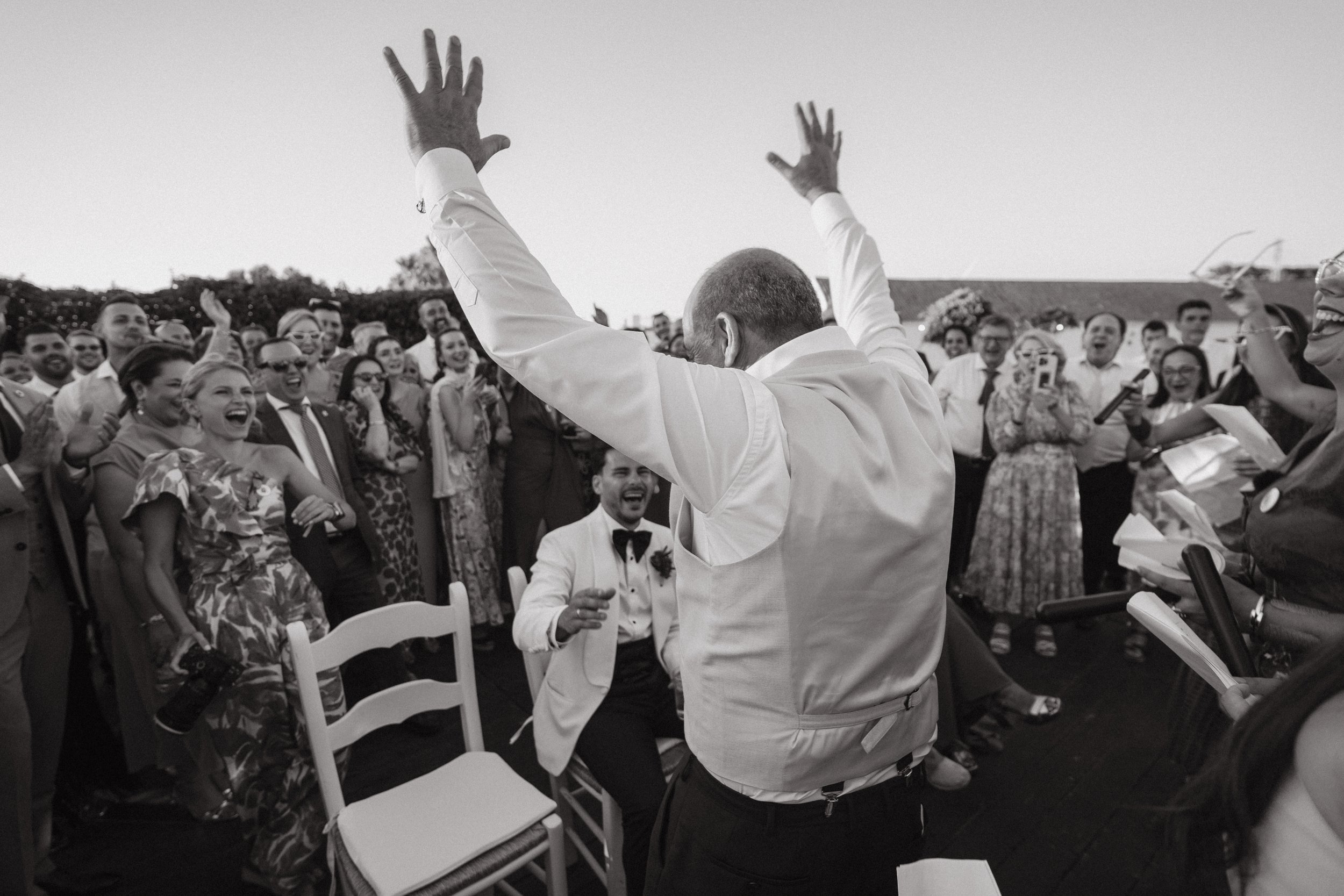 Grupo de personas en una boda en Dehesa Bolaños, una finca en CÁDIZ, riendo y disfrutando, con un hombre en el centro levantando las manos, foto en blanco y negro.