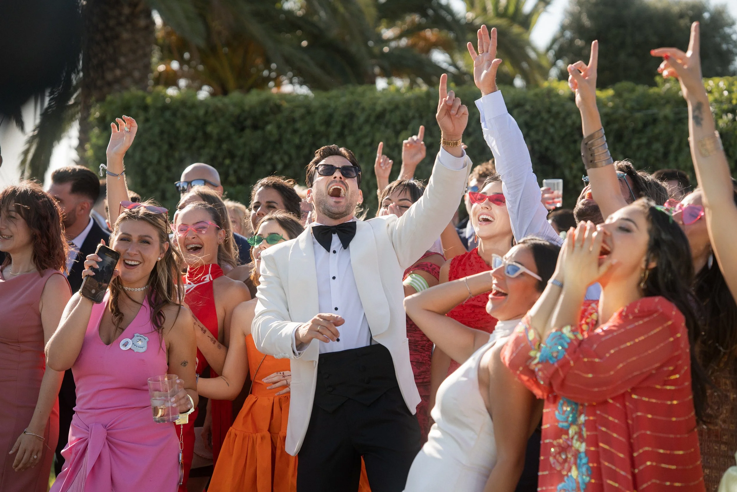 Grupo de personas celebrando y disfrutando en un evento al aire libre con sonrisas y gestos de alegría, usando ropa colorida y accesorios de moda.