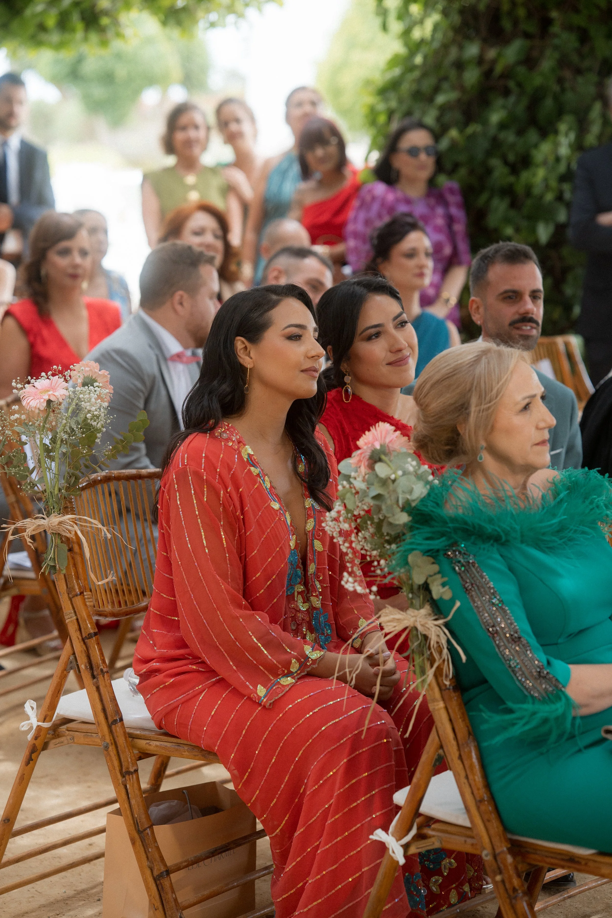 Grupo de personas asistiendo a una ceremonia de boda en un espacio abierto, con muchas flores decorativas y vestimenta elegante.