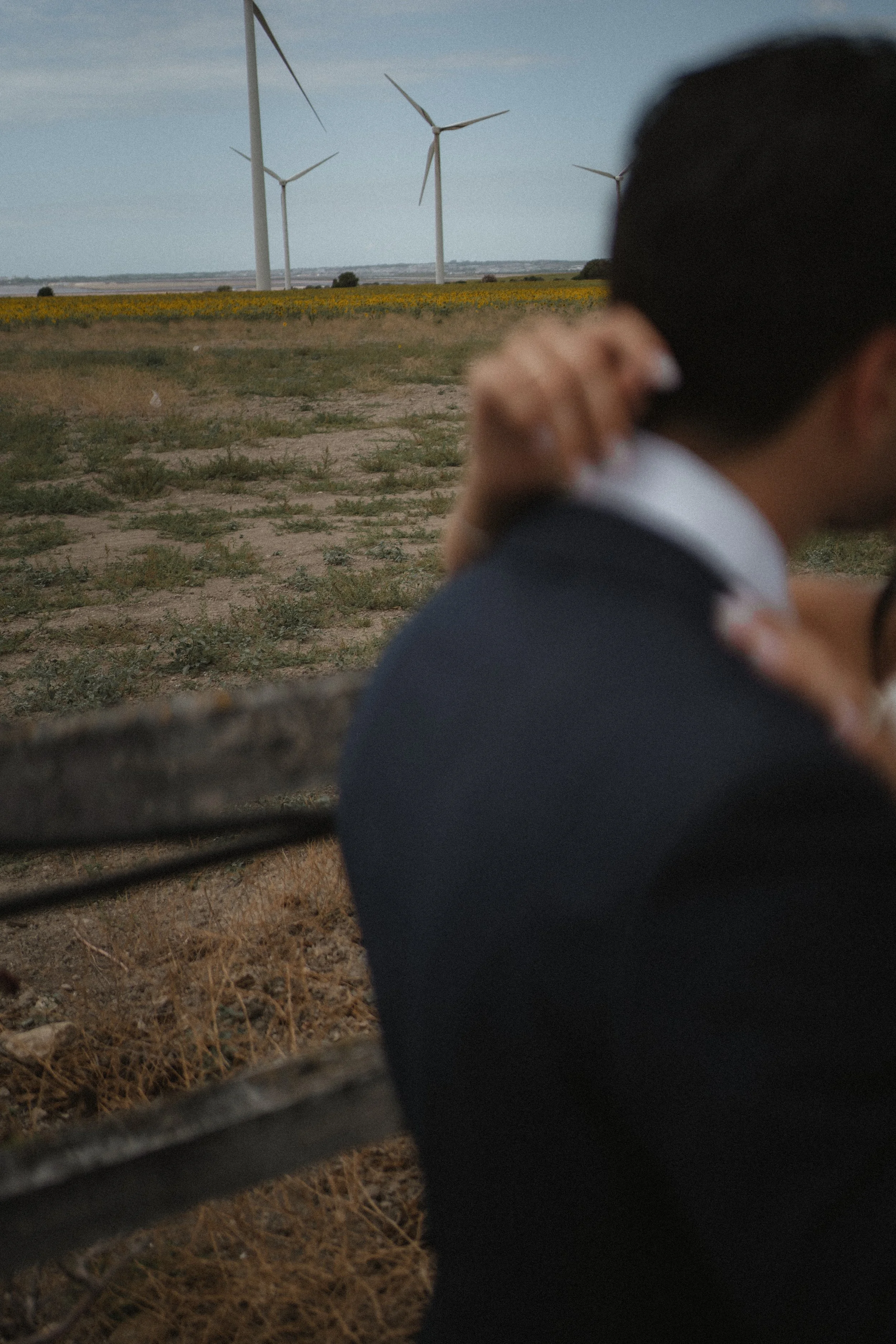 Pareja abrazada en un entorno rural con molinos de viento en el fondo.