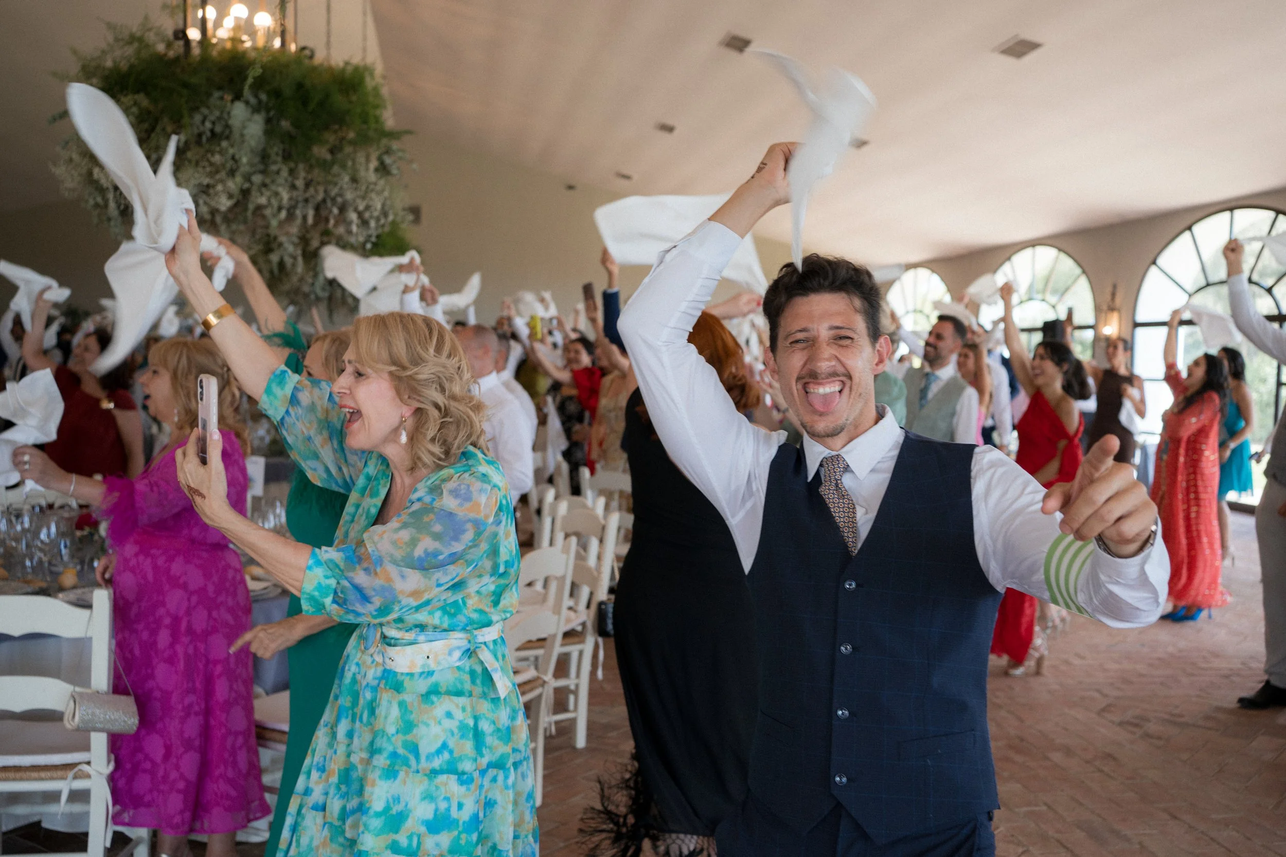 Hombre y mujer en celebración en una fiesta, lanzando servilletas al aire, con muchas personas en el fondo en un ambiente alegre y festivo