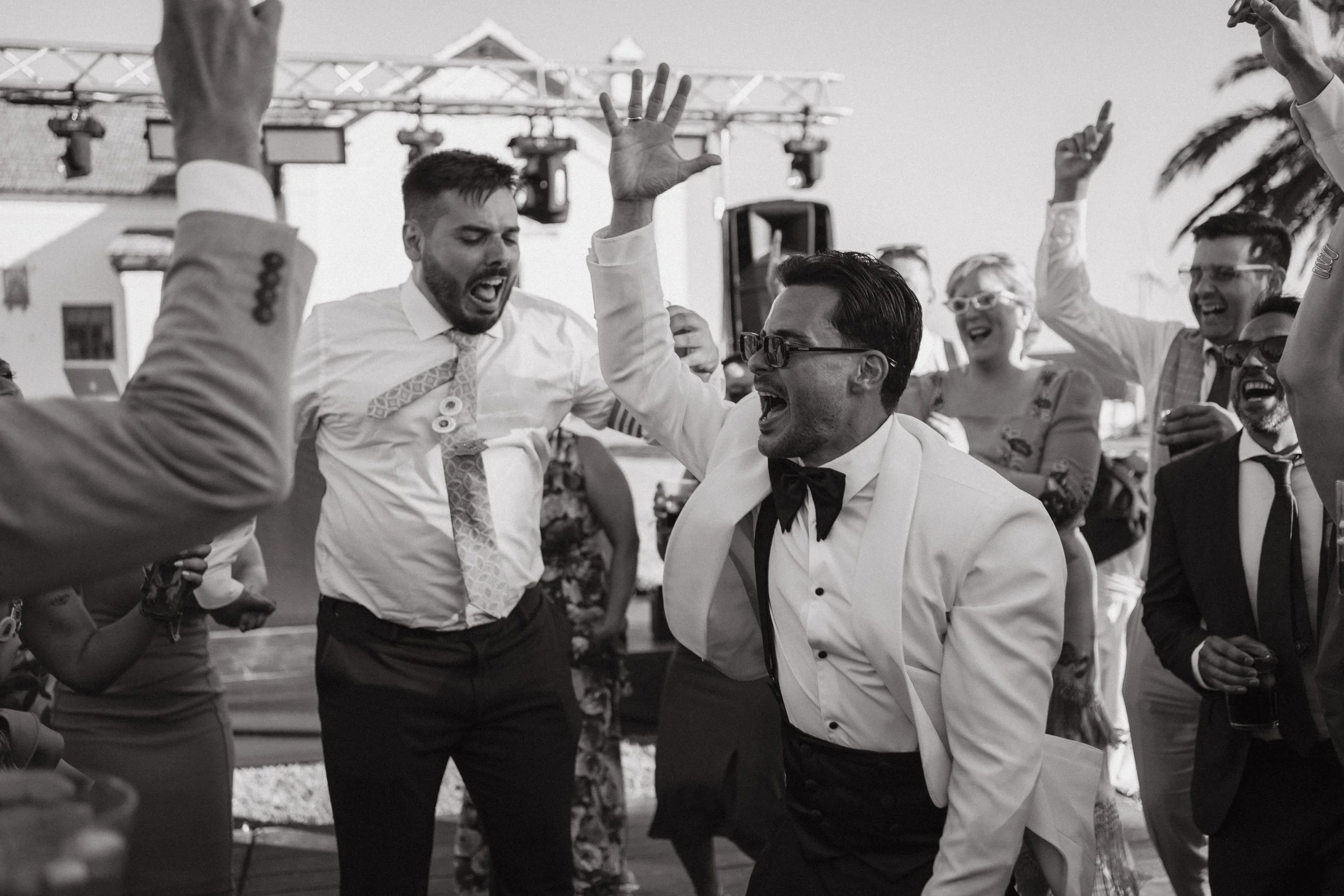 Personas bailando y disfrutando en una fiesta al aire libre, algunos con ropa formal, en un ambiente festivo.