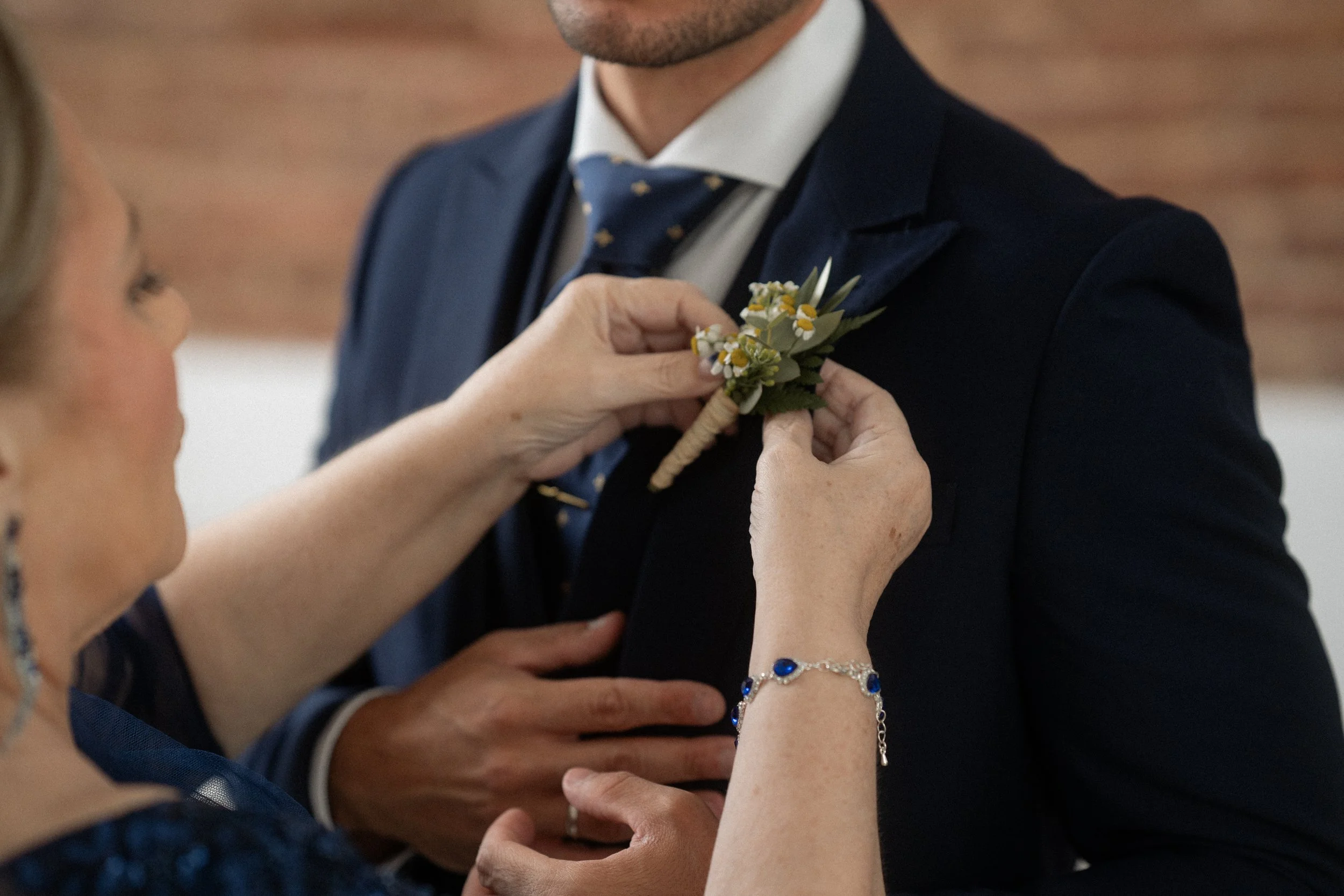 Una mujer coloca un bouton de flores en el saco del novio en una boda.