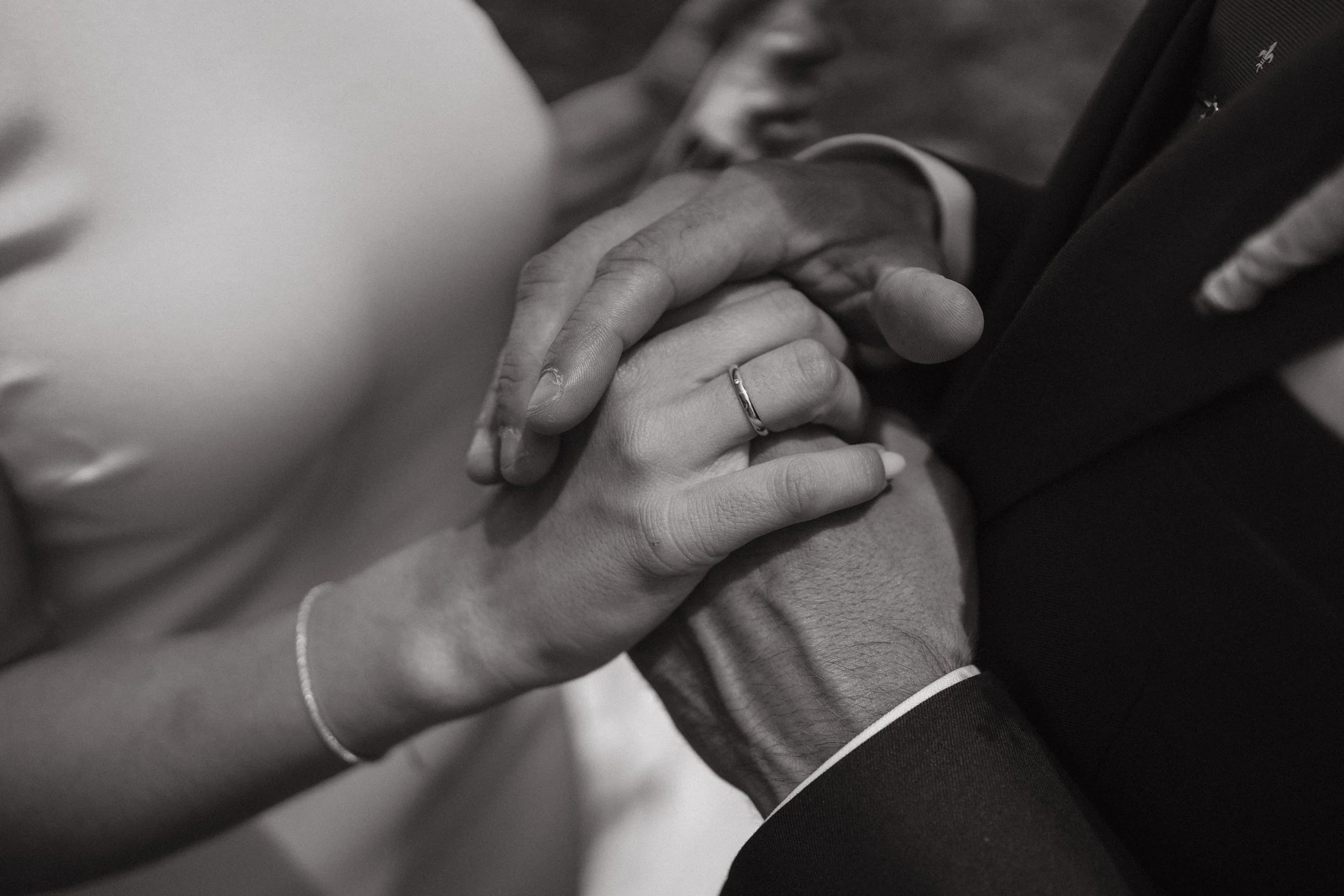 Primer plano de las manos entrelazadas de una pareja en una ceremonia, con un anillo en el dedo de una de las manos.