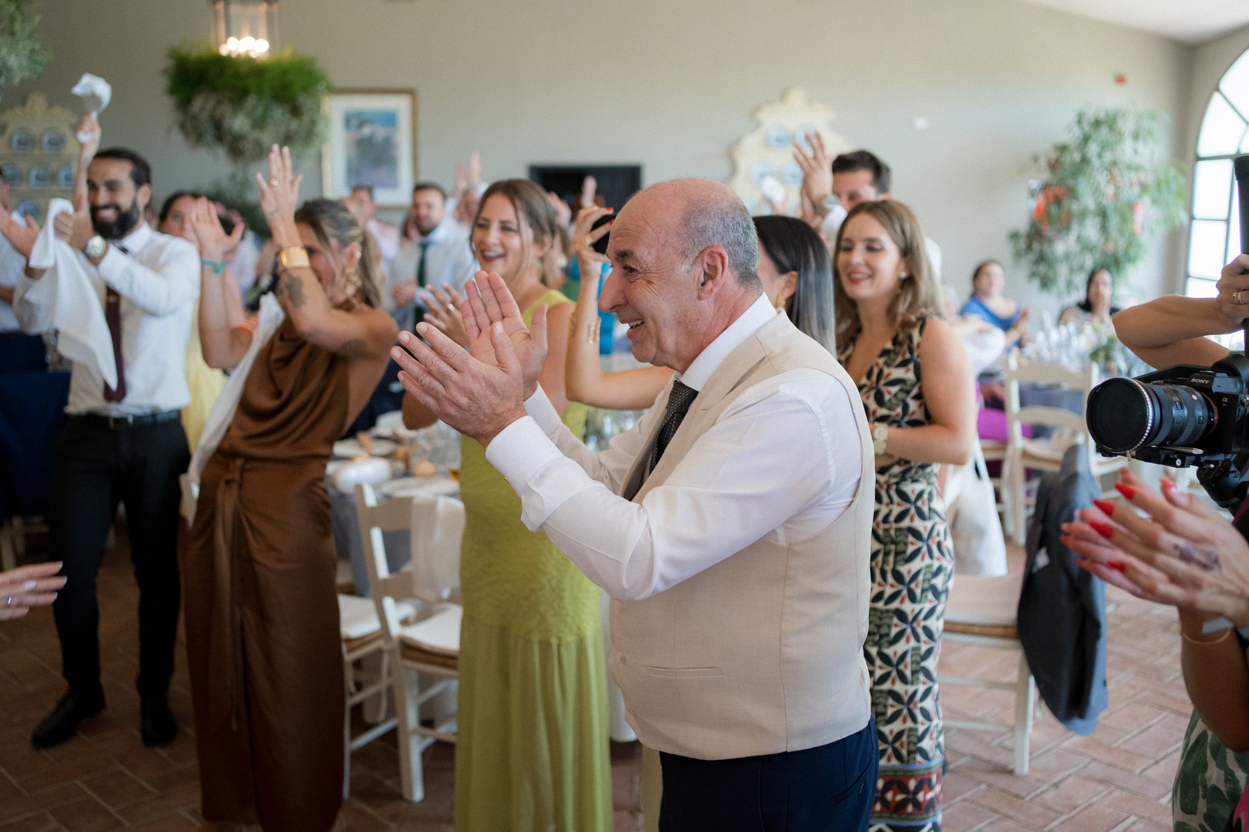 Grupo de personas en celebración, algunas aplaudiendo y sonriendo, en un evento social en interiores con decoración elegante.