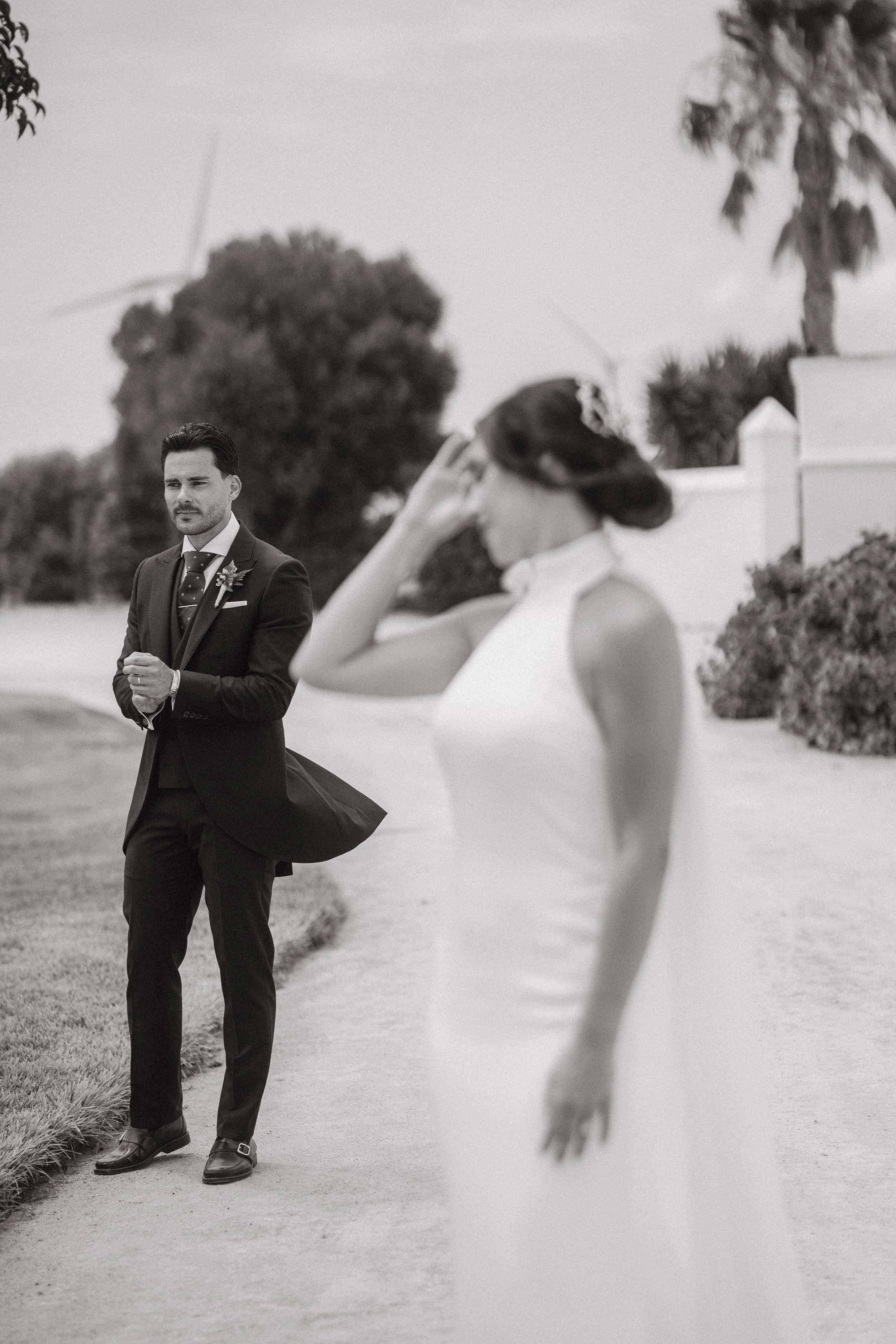 Una pareja en una ceremonia de bodas al aire libre, la mujer con vestido blanco y el hombre con traje oscuro, en un entorno natural con algunas plantas y árboles, en una foto en blanco y negro.