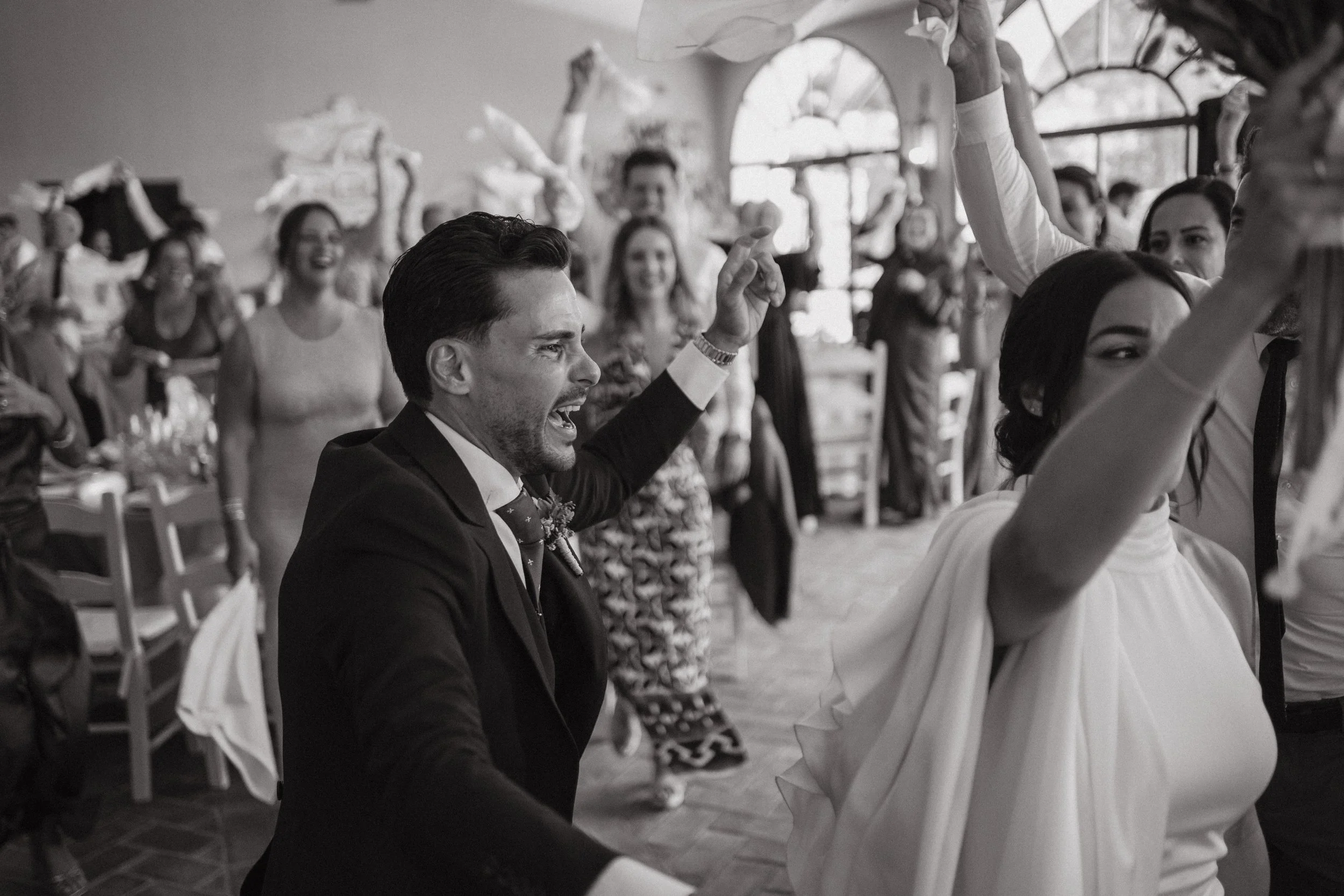 Pareja bailando en una fiesta, rodeada de personas que disfrutan, en un ambiente festivo, con decoraciones y mesas