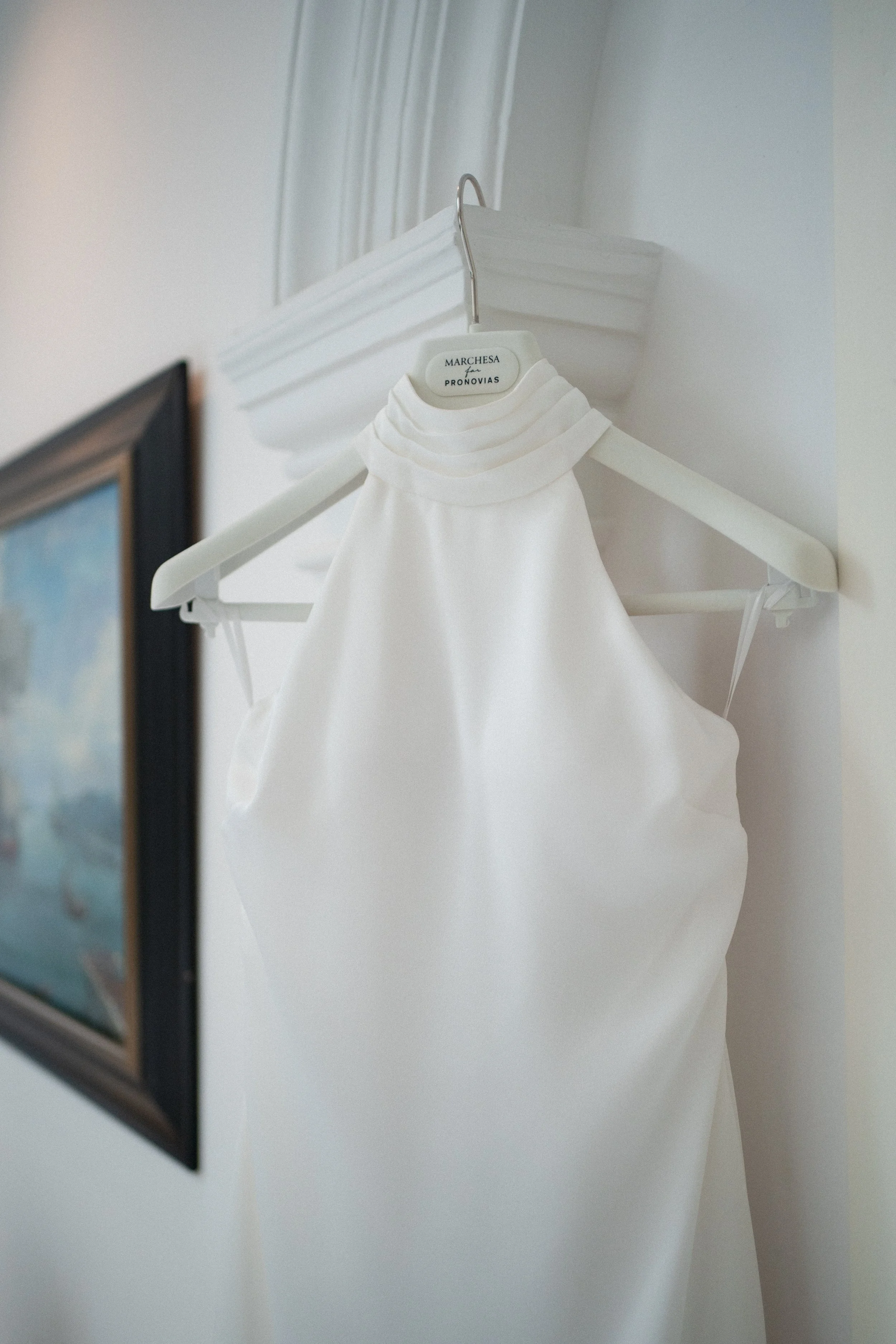 Vestido blanco de la marca pronovias colgado en una percha en la pared en hotel de Cádiz.