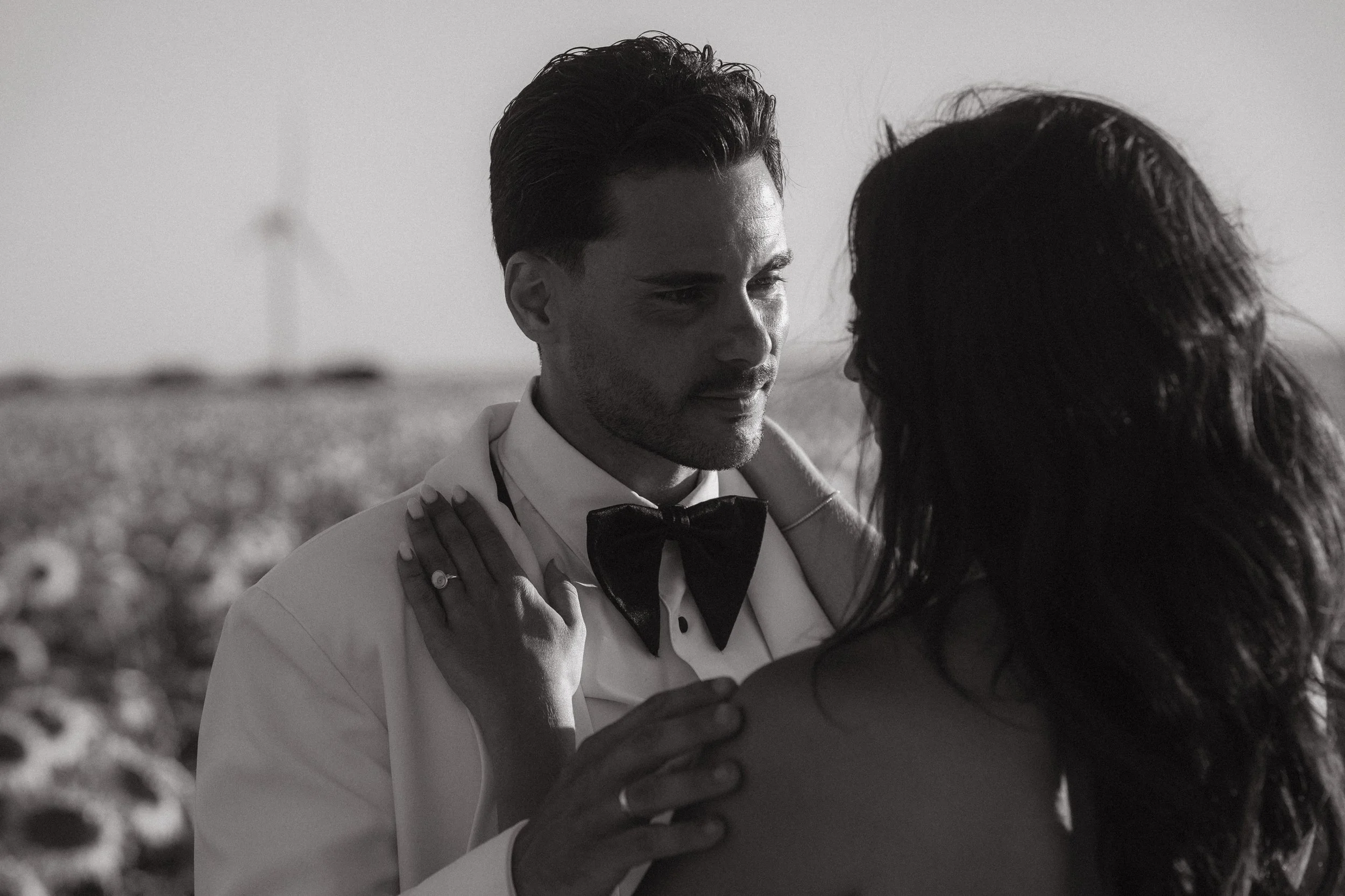 Una pareja abrazada en un campo de flores, el hombre viste de esmoquin y la mujer tiene el cabello suelto.