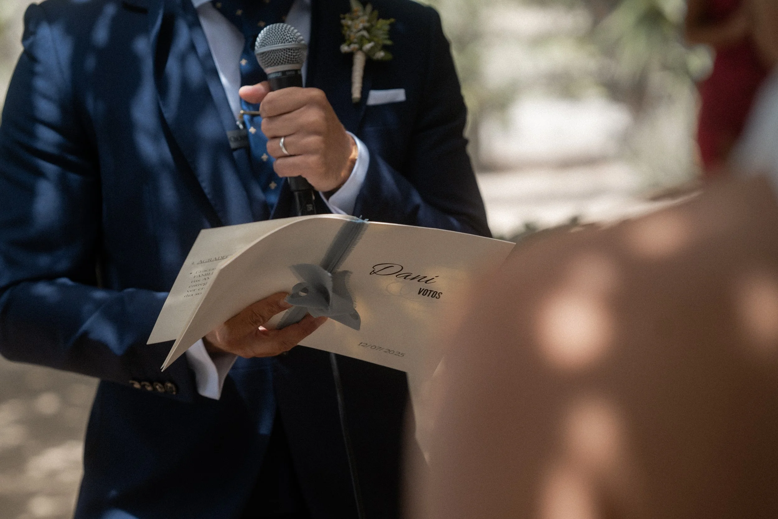 Persona en traje azul leyendo votos de una libreta durante una ceremonia en exteriores de la finca DEHESA BOLAÑOS.
