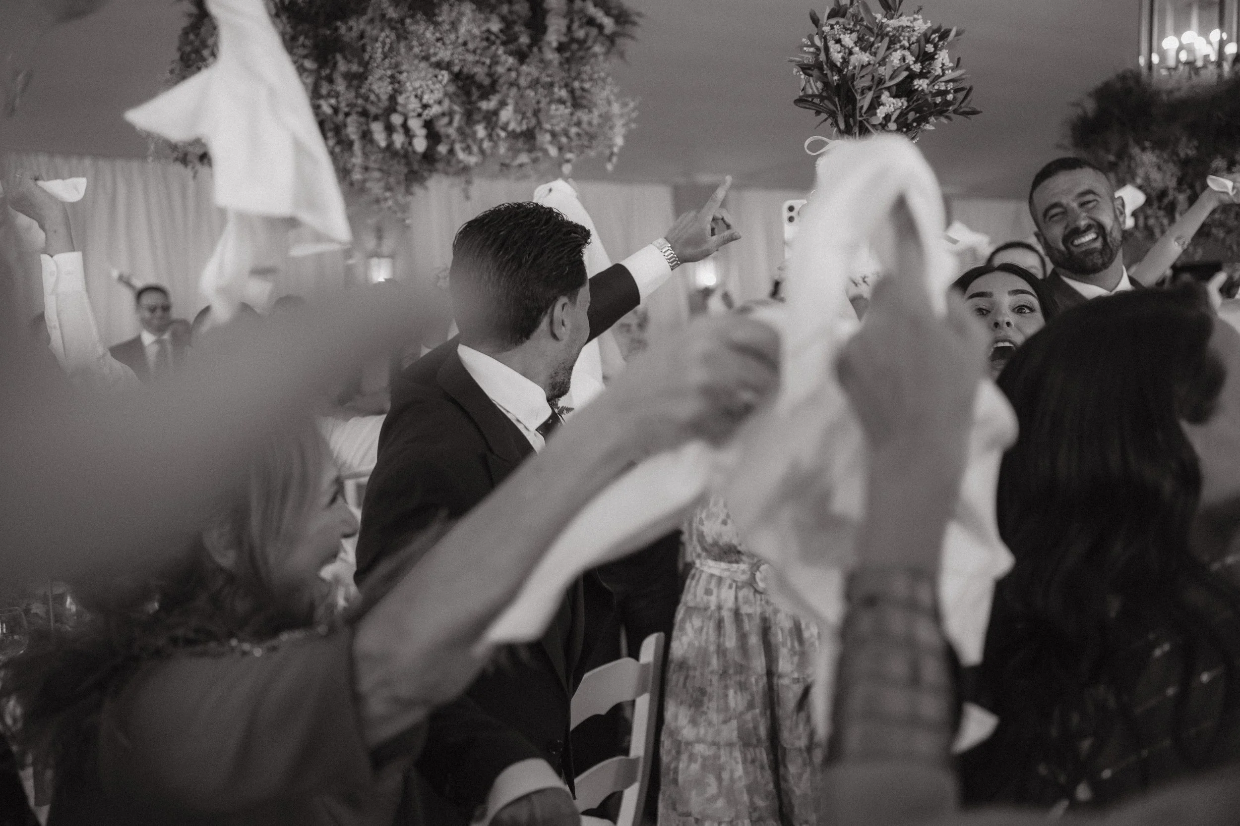 Celebración en una boda con invitados bailando y sonriendo en un ambiente elegante decorado con flores y luces.