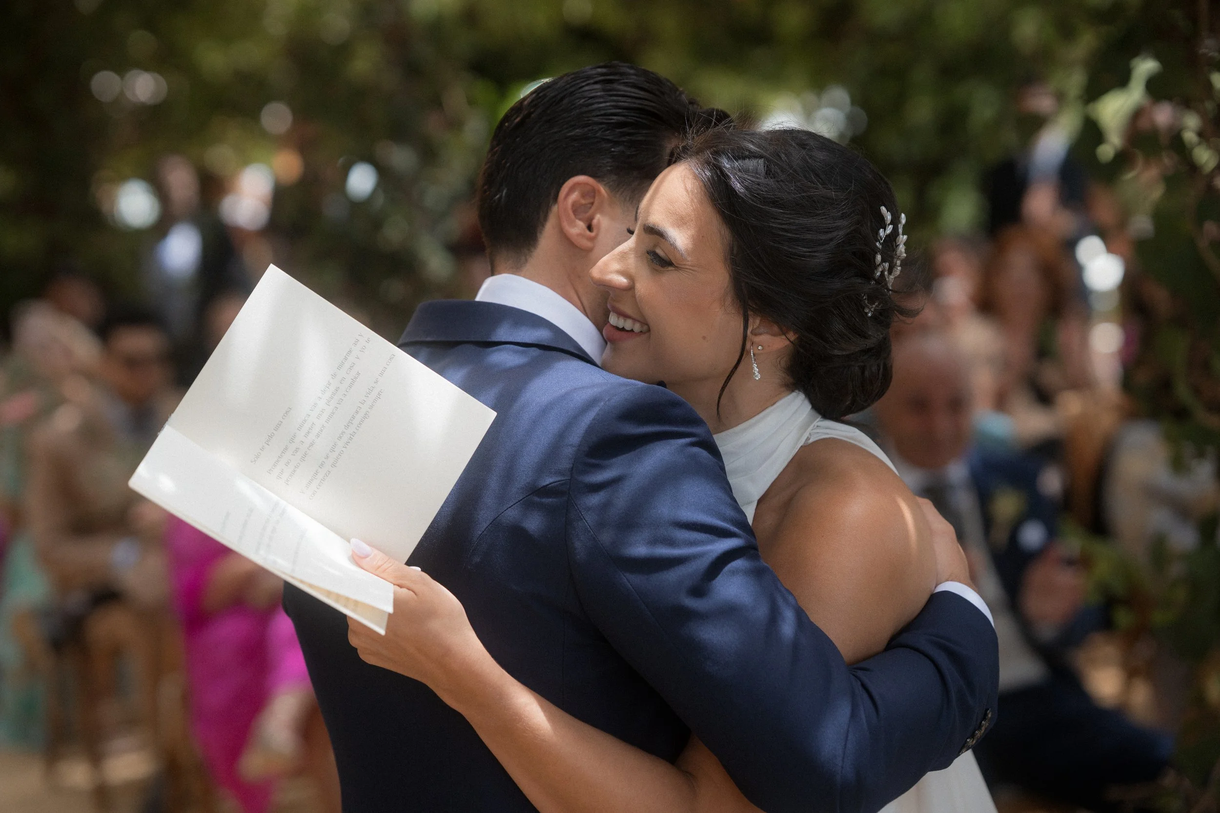 Pareja de novios besándose en su boda, con invitados en el fondo.