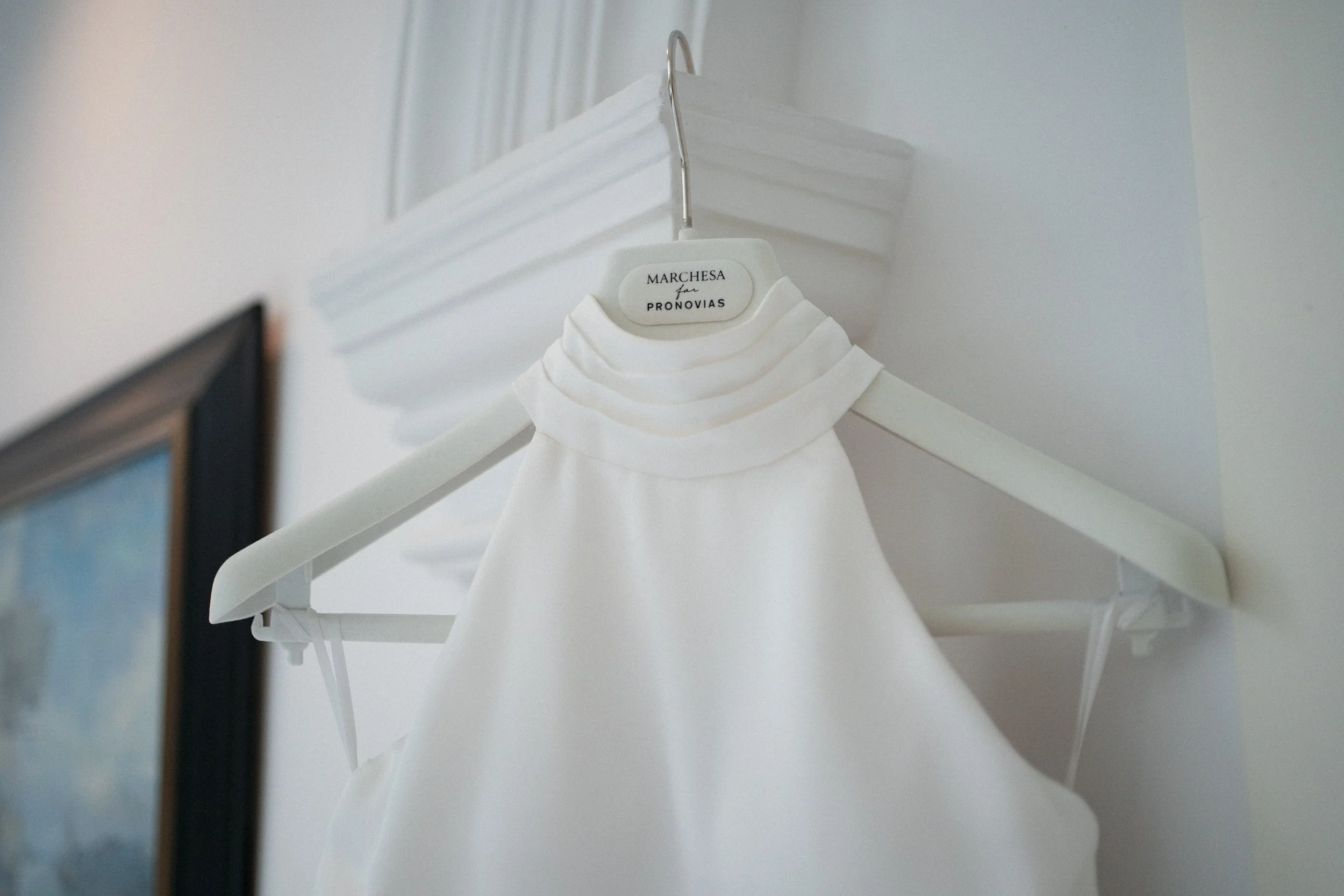 Vestido blanco de PRONOVIAS  para novia colgado en una percha en una pared blanca con moldura